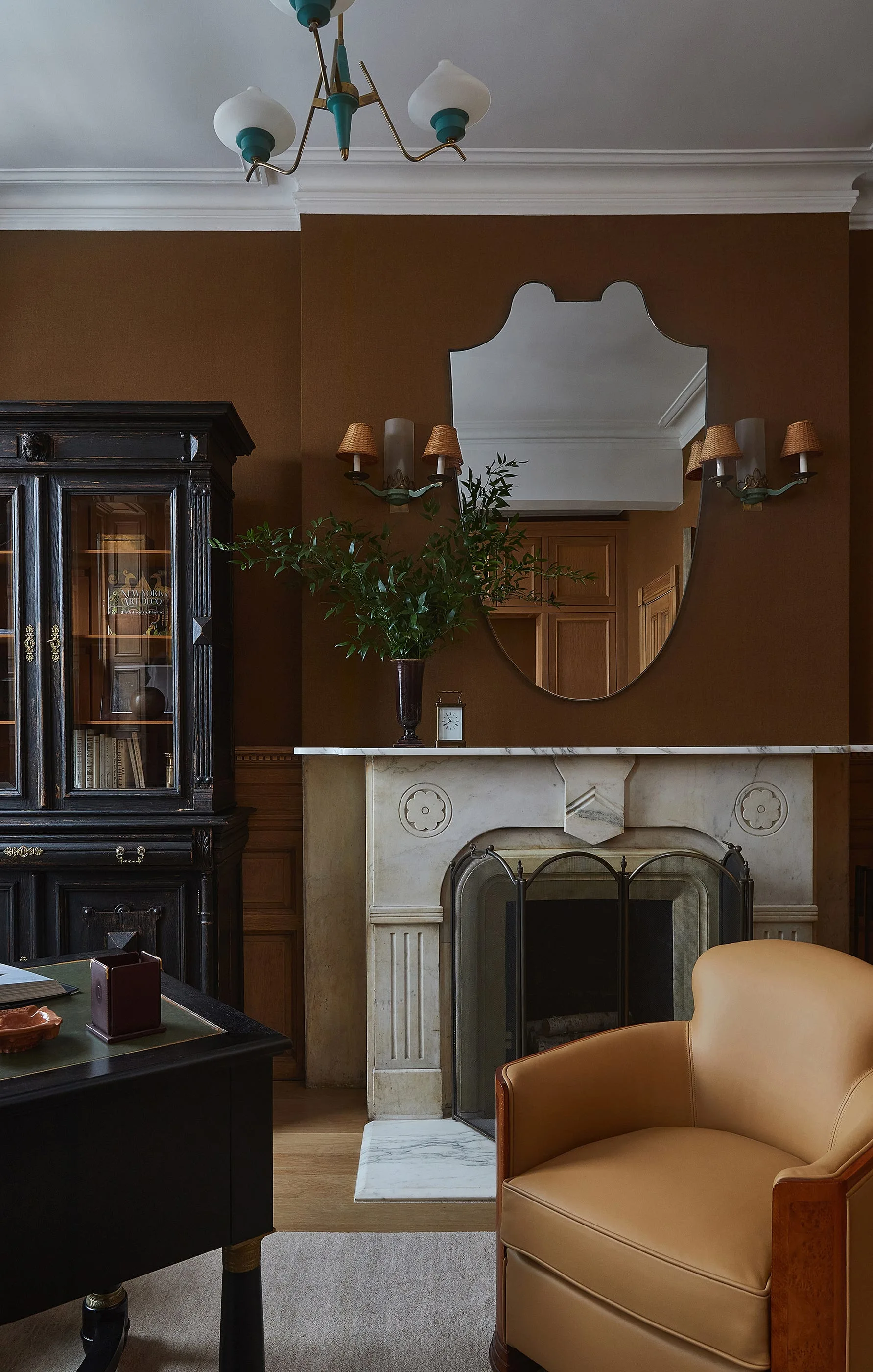 A traditional study featuring a white carved marble fireplace, a tan leather armchair, and a dark wooden cabinet against dark brown walls.