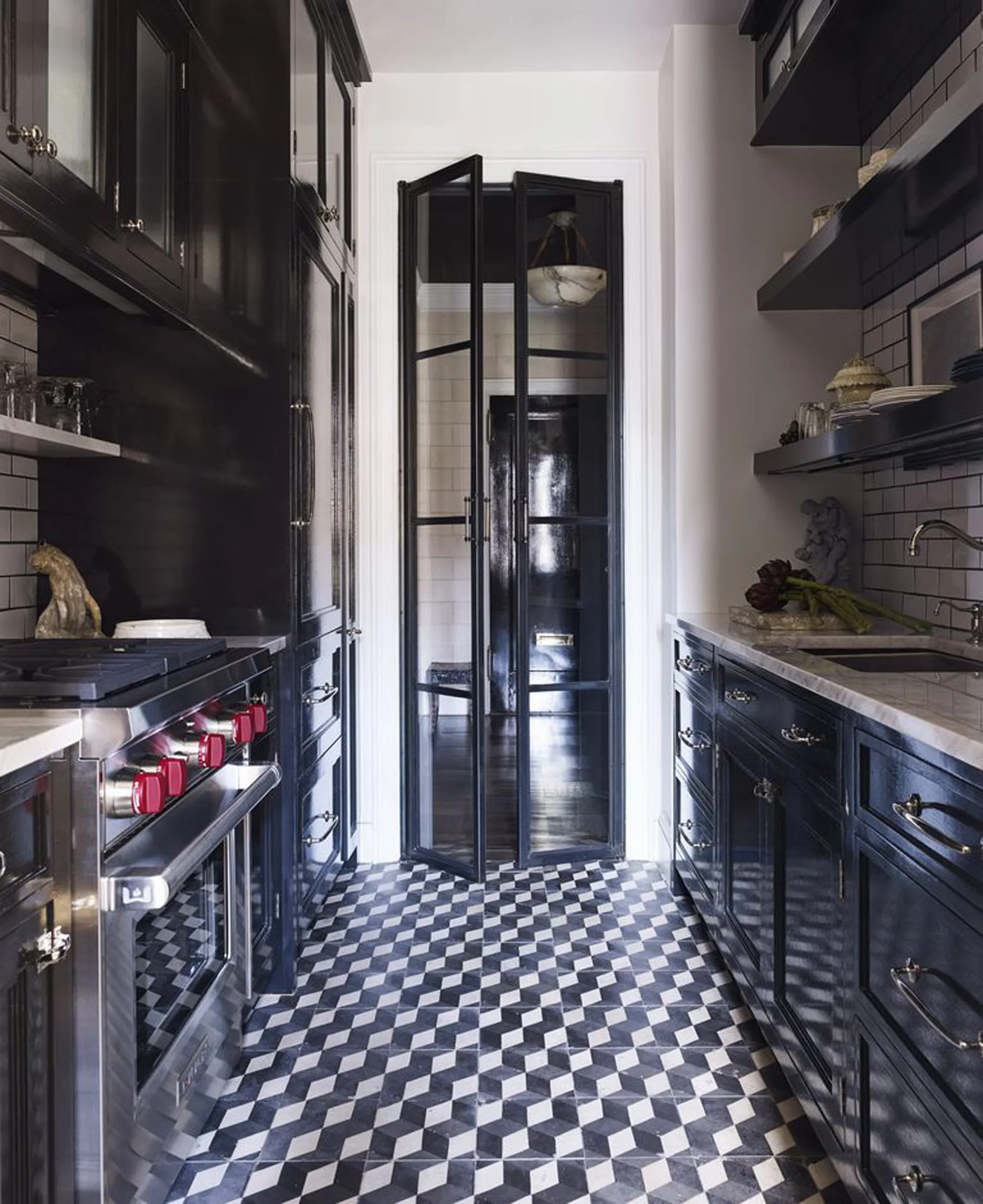 A galley kitchen featuring glossy black cabinets, white countertops, a subway tile backsplash, and a black and white geometric patterned floor.