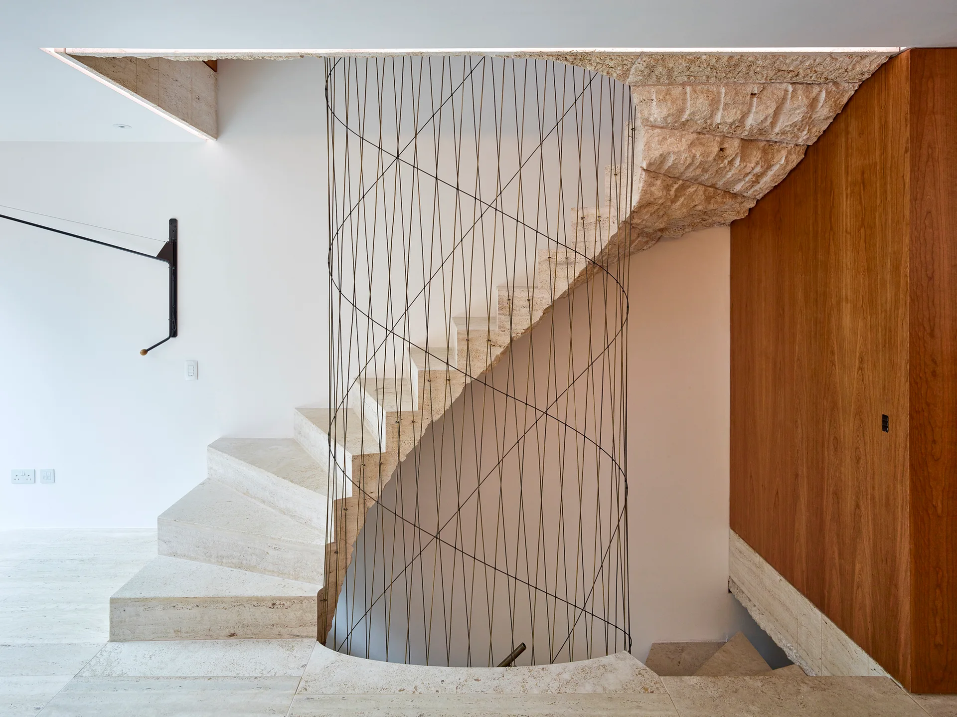 A curved stone staircase features a vertical tension wire balustrade, white plaster walls, and warm wood wall paneling.