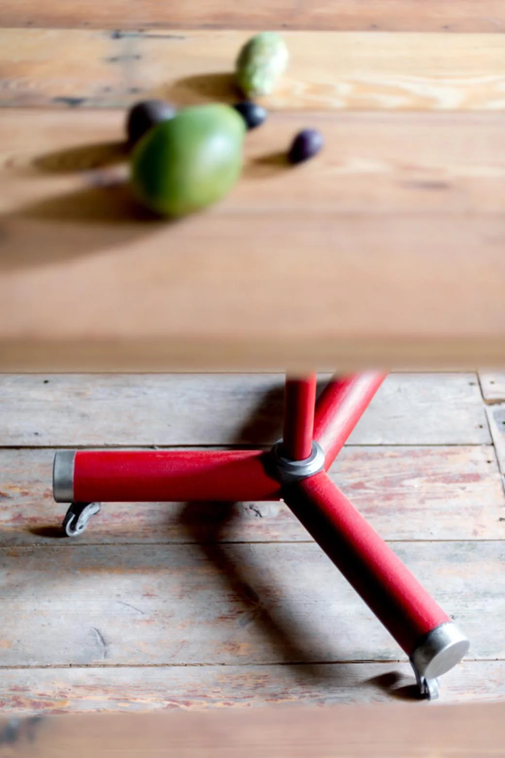 A red industrial table base with metal legs and small caster wheels sits on a distressed wood plank floor.