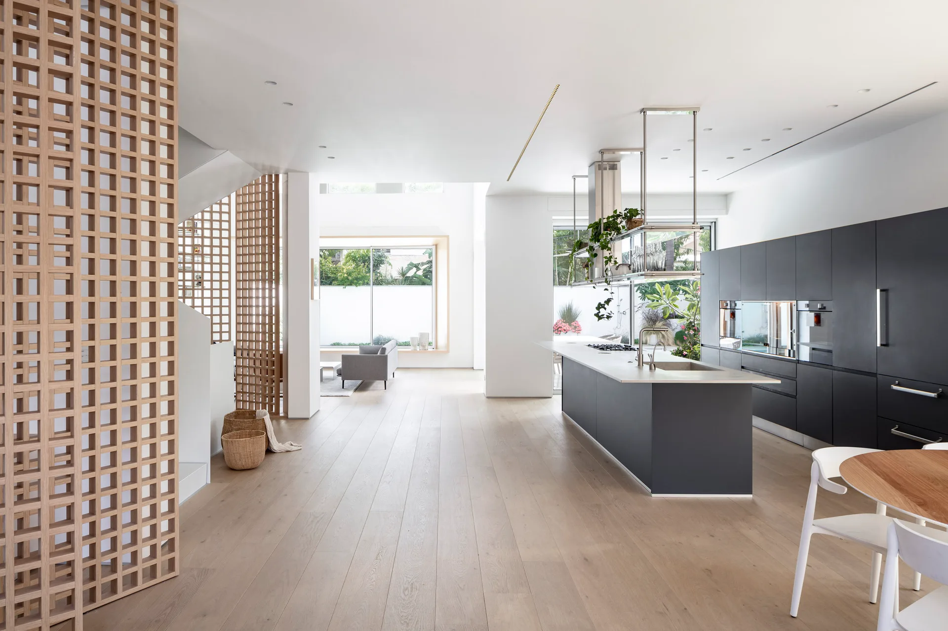 An open-concept kitchen and living space with dark charcoal cabinets, a central island, light oak flooring, and tall wooden lattice divider screens.
