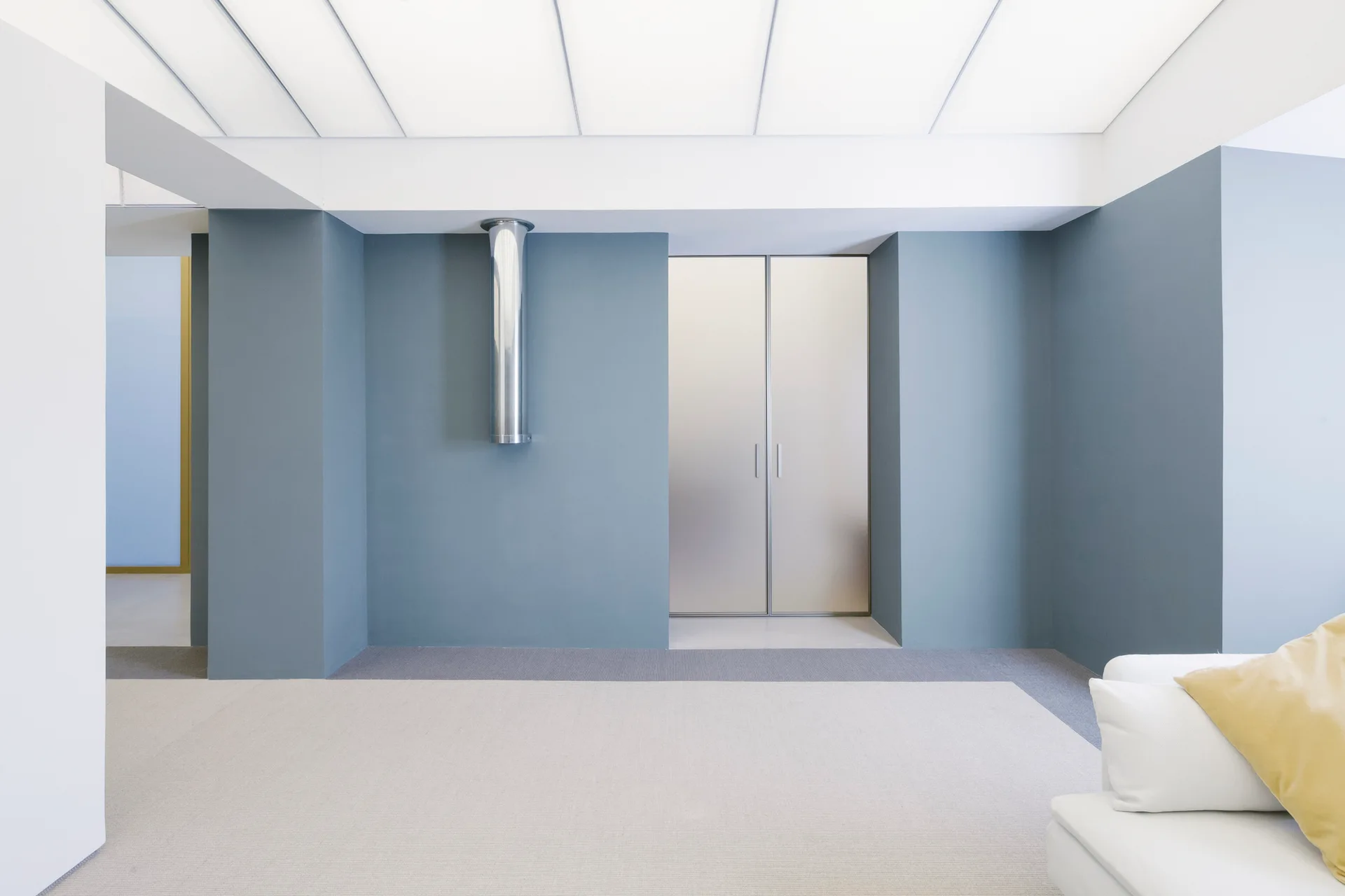 A minimalist living room features smooth slate blue walls, recessed frosted glass closet doors, a white floor, and a partial view of a white sofa.