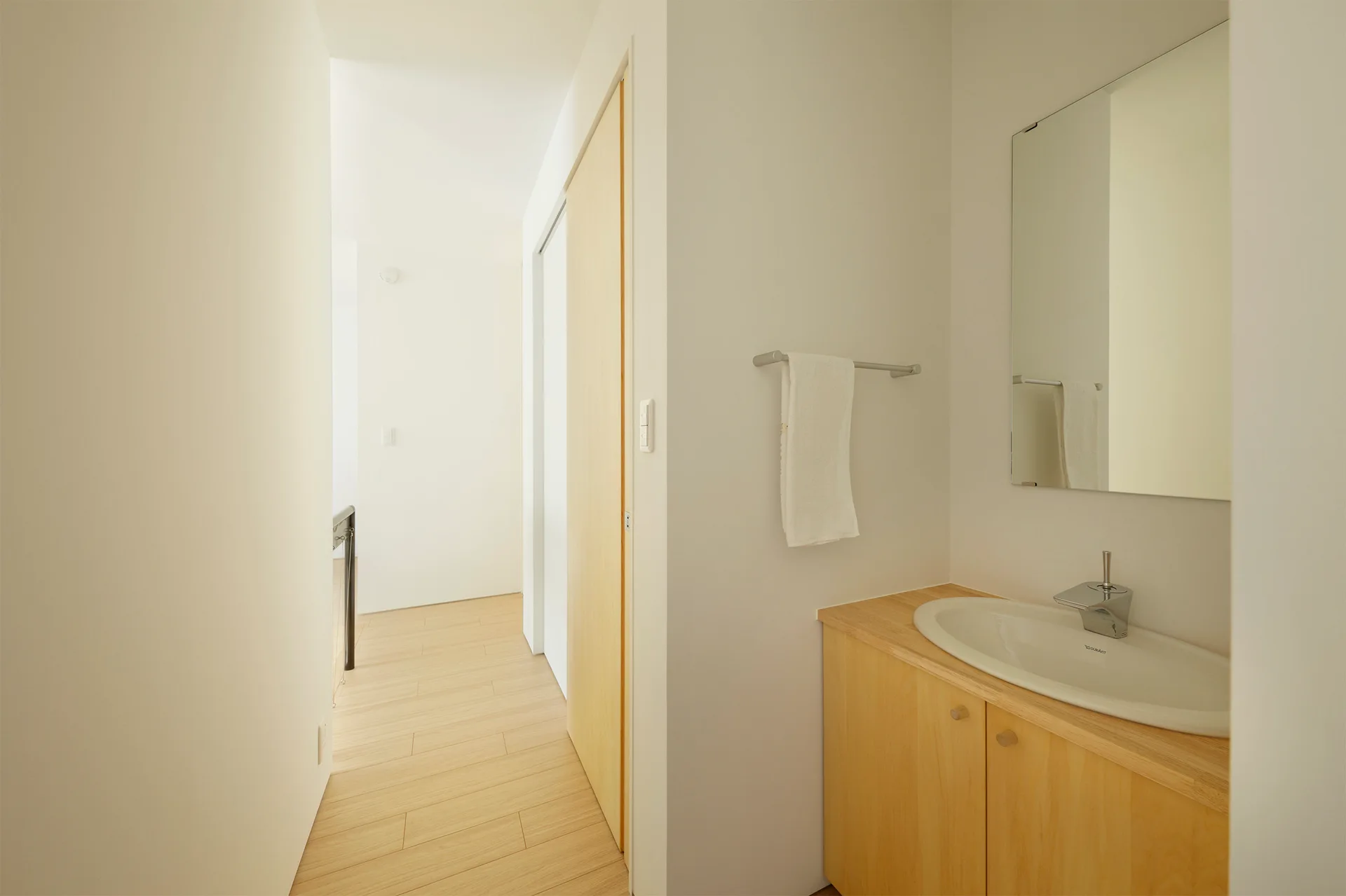 A minimalist powder room niche features a light wood vanity with a white oval sink, a rectangular mirror, and matching light wood floors.