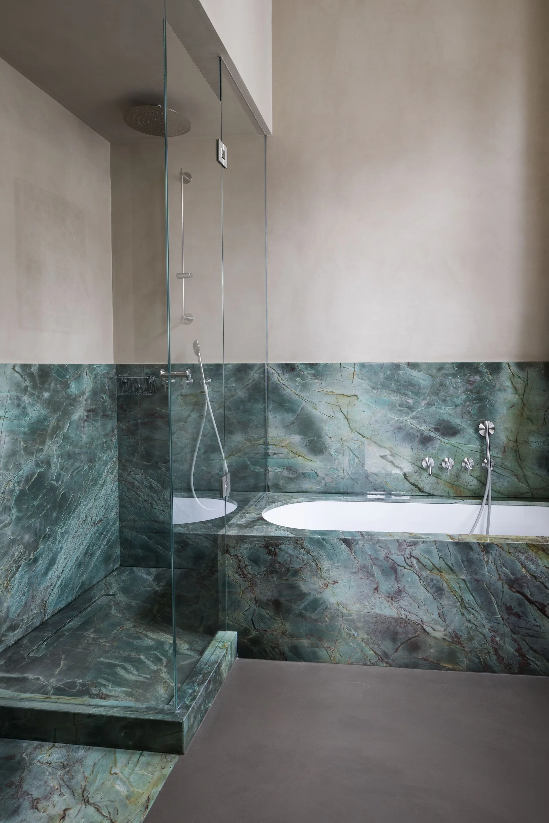 A modern bathroom features a walk-in shower with a frameless glass panel next to an integrated bathtub, both surrounded by green veined marble.
