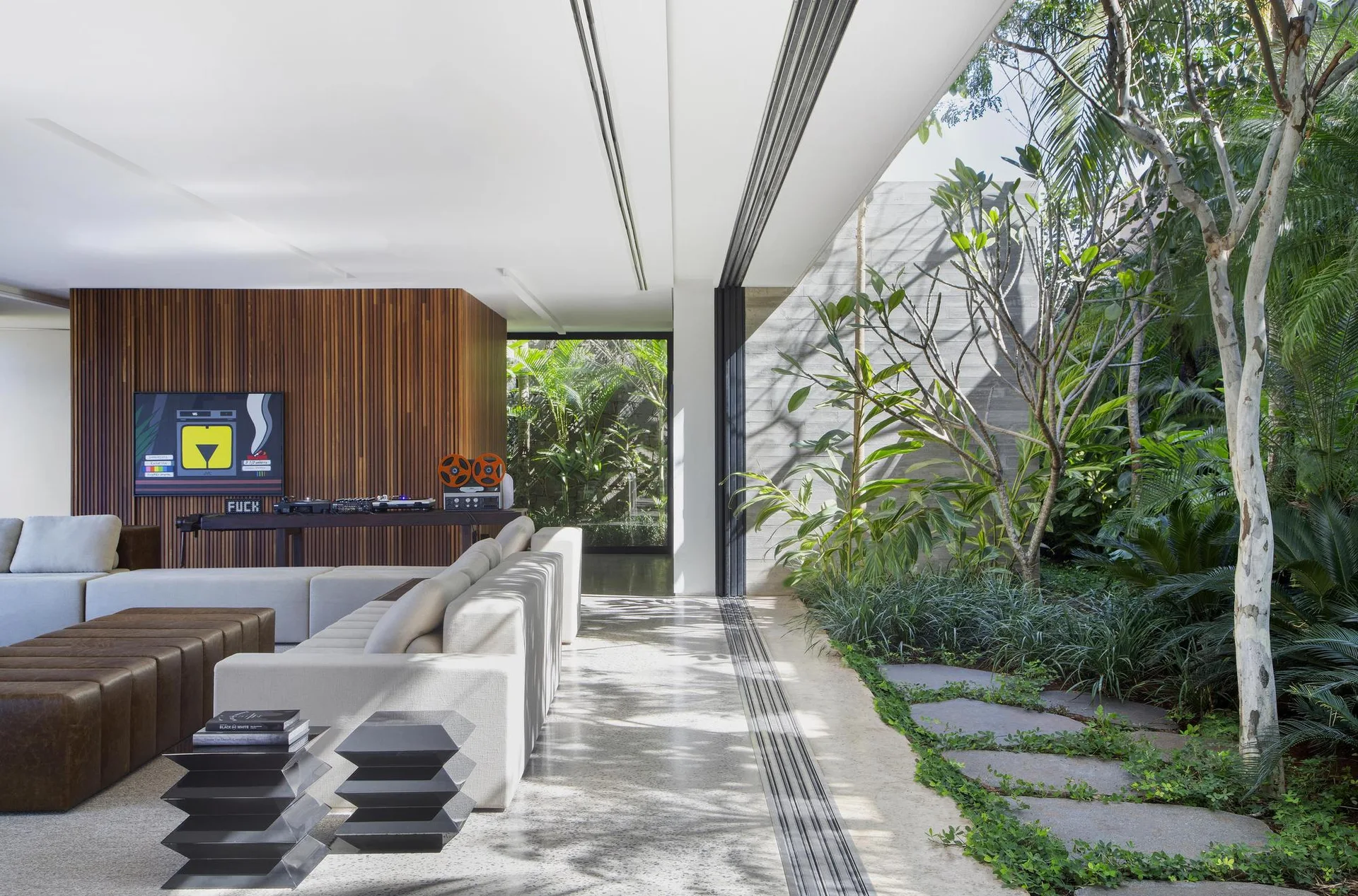 A modern living room features a modular cream sofa and a wood slat wall next to fully opened sliding glass doors leading to a lush garden.