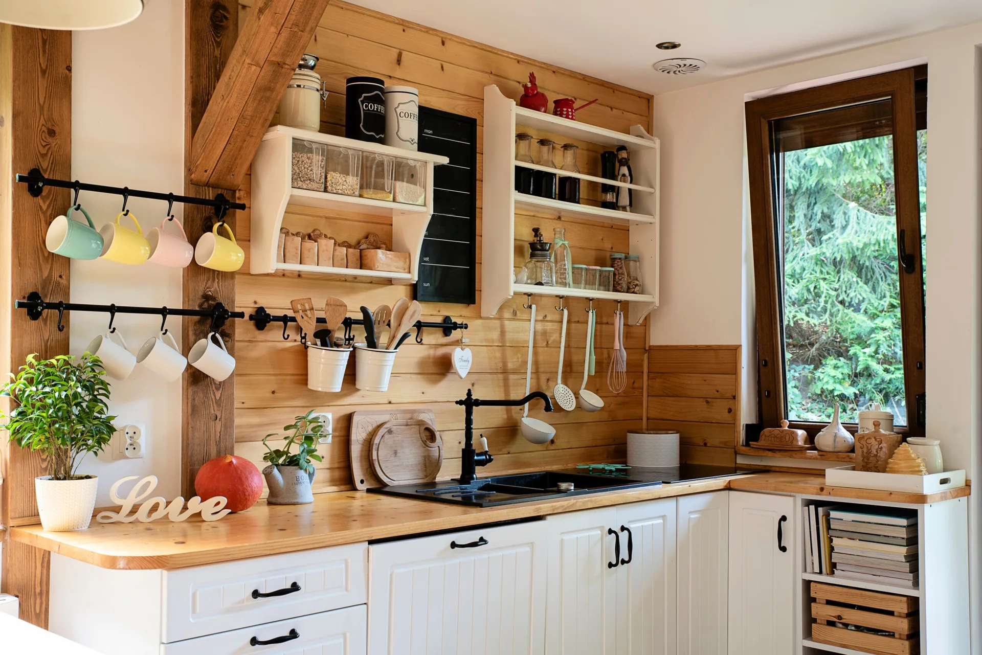 A farmhouse kitchen featuring white base cabinets, a natural wood countertop, horizontal wood plank walls, and white open shelving with hanging utensils.