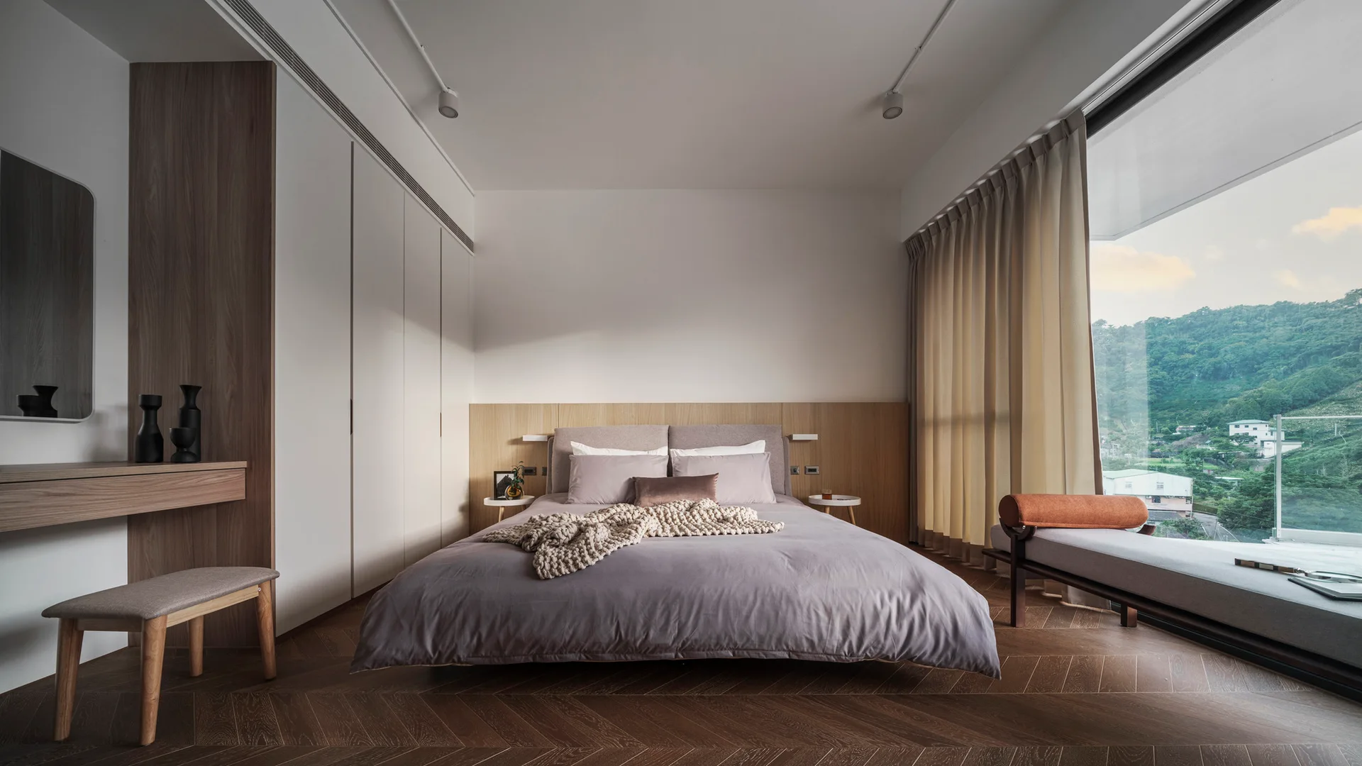 A minimalist bedroom featuring a low-profile bed, a wood panel headboard, and a large window showcasing mountain views.
