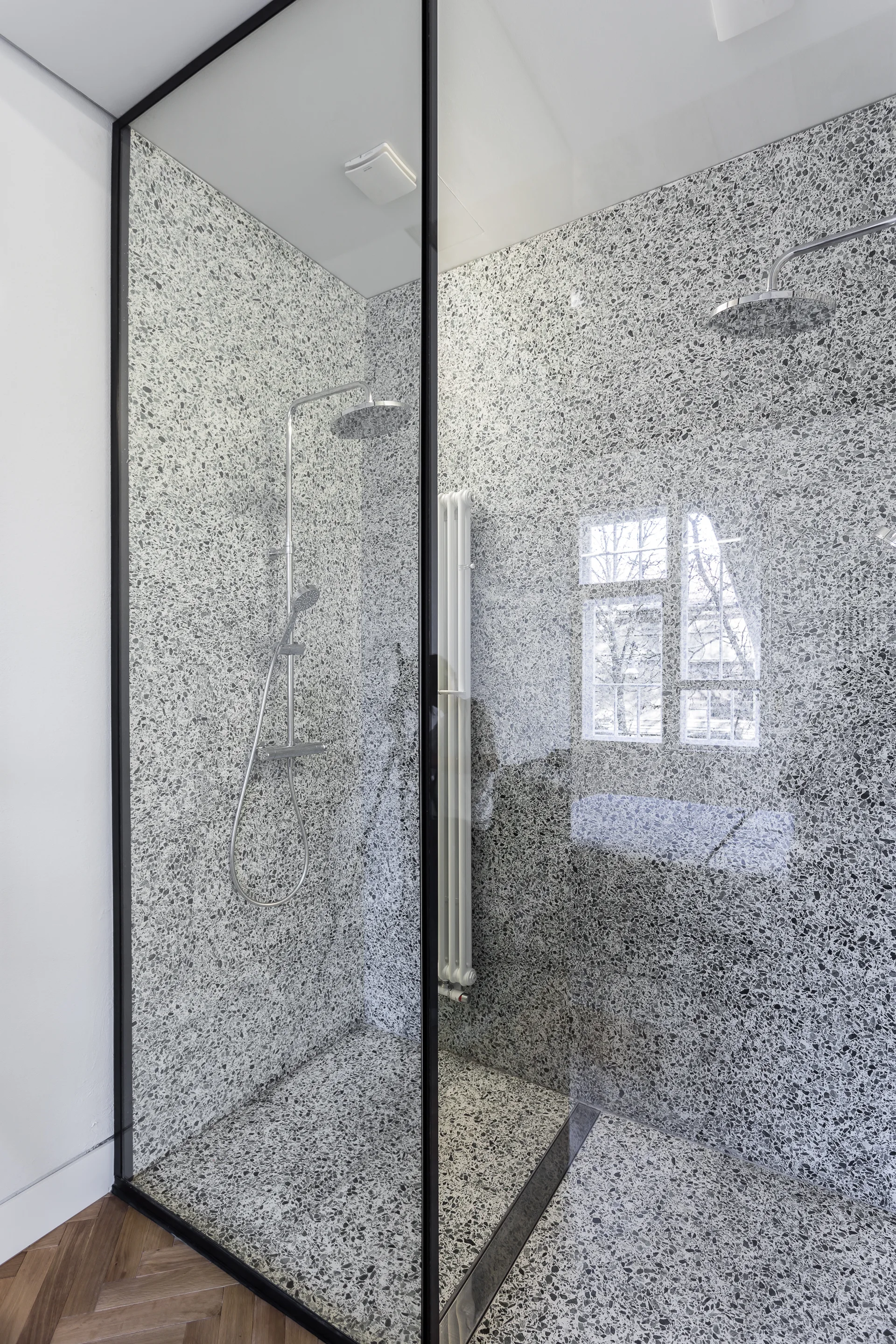 A walk-in shower features grey terrazzo tiled walls and flooring, a black-framed glass enclosure, and chrome plumbing fixtures.