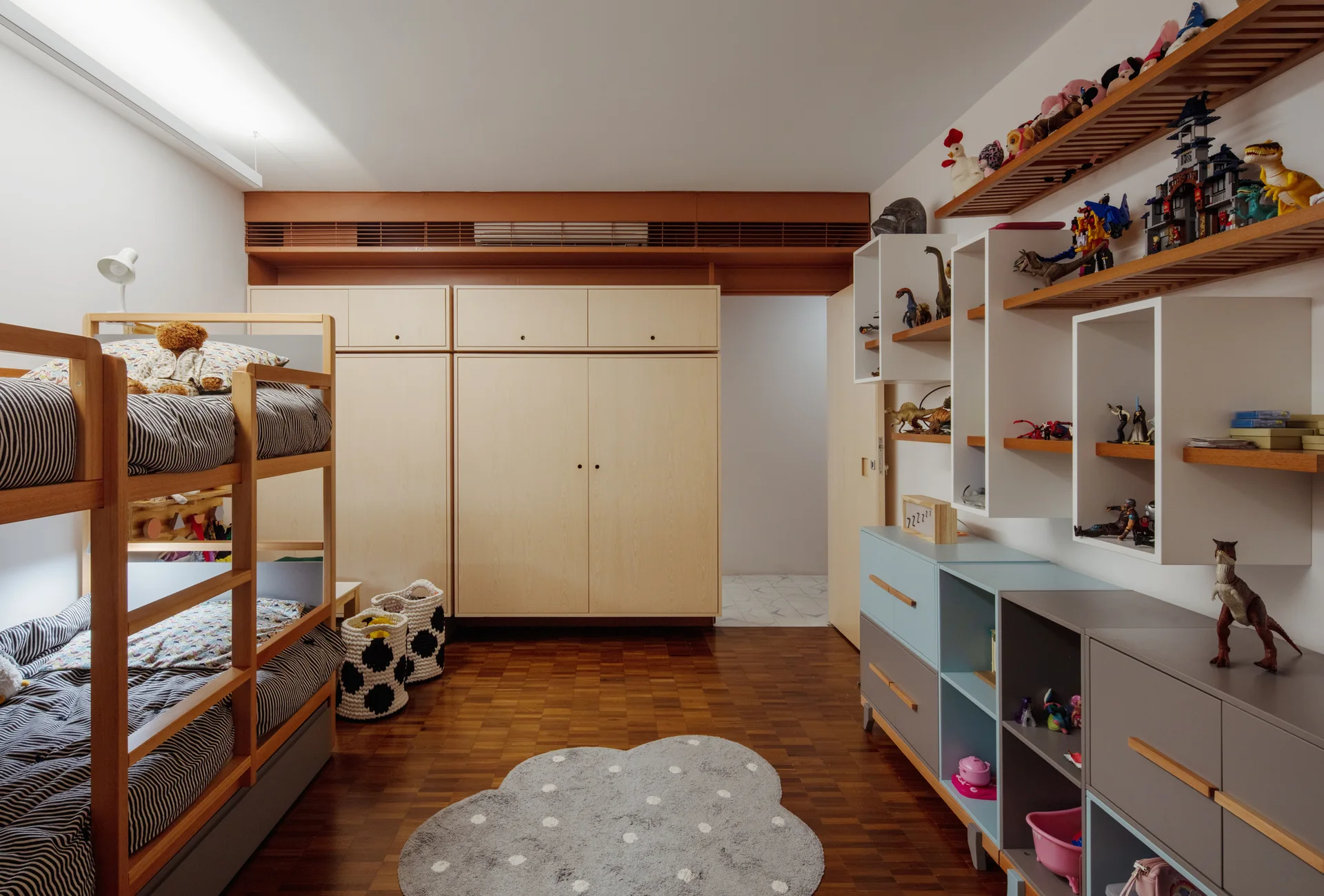 A children's bedroom featuring a wooden bunk bed, light wood built-in wardrobes, a parquet floor with a cloud rug, and toy shelving.