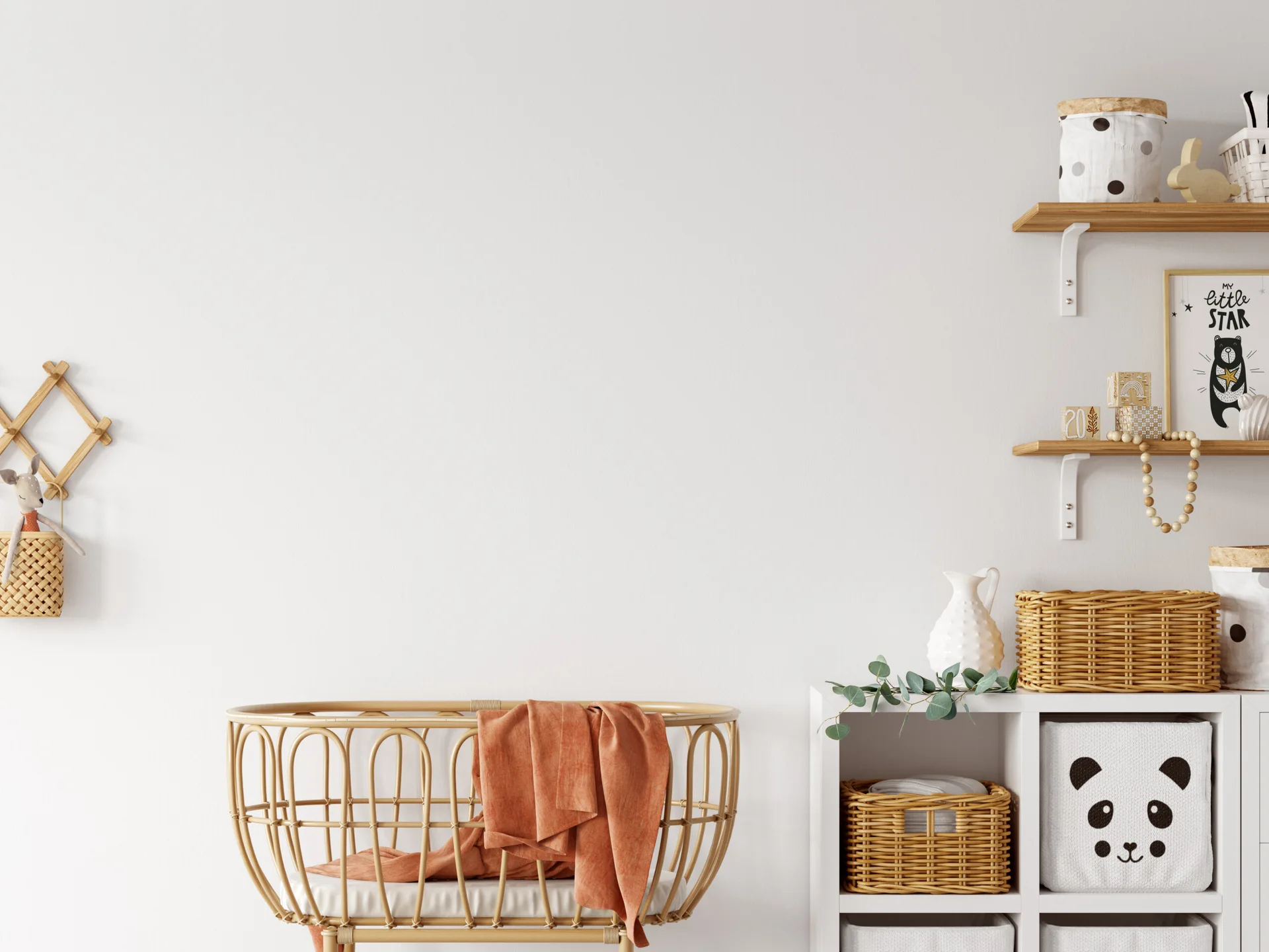 A light-filled nursery features a central rattan bassinet with a terracotta drape, a white cube organizer, and wooden shelves against a plain white wall.
