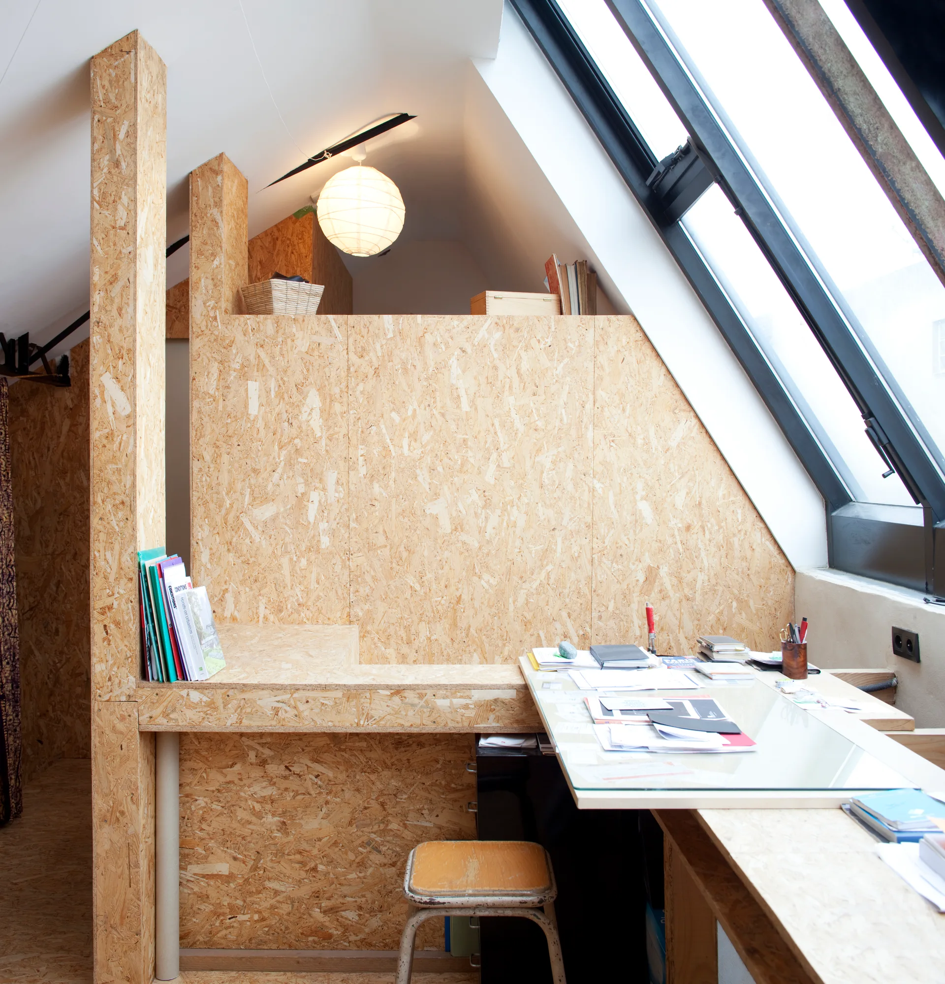A minimalist attic home office features walls, floors, and a built-in desk made from OSB panels under a sloped ceiling with a large skylight.