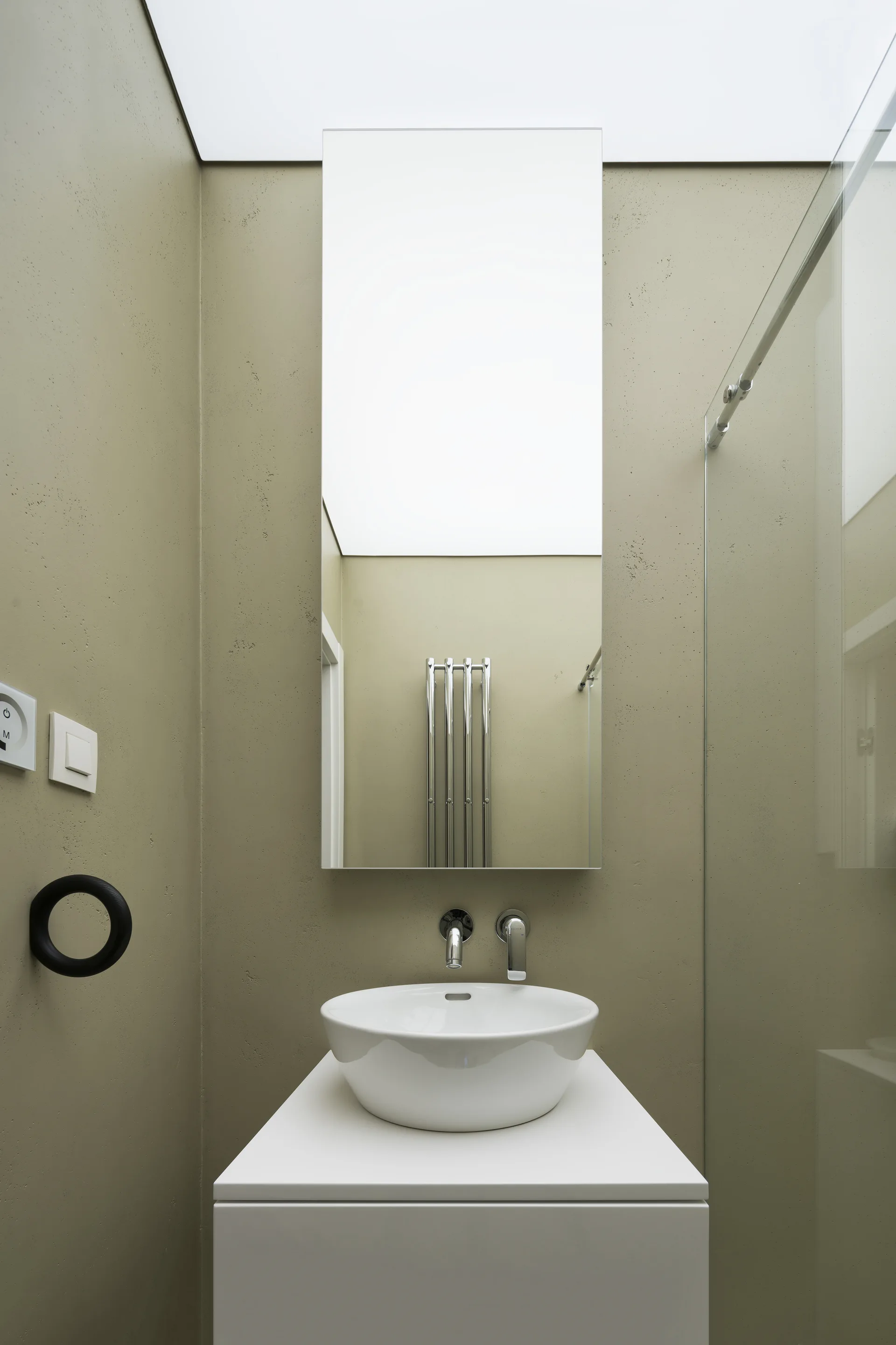 A minimalist white vanity with a vessel sink and tall frameless mirror set against textured olive green walls.