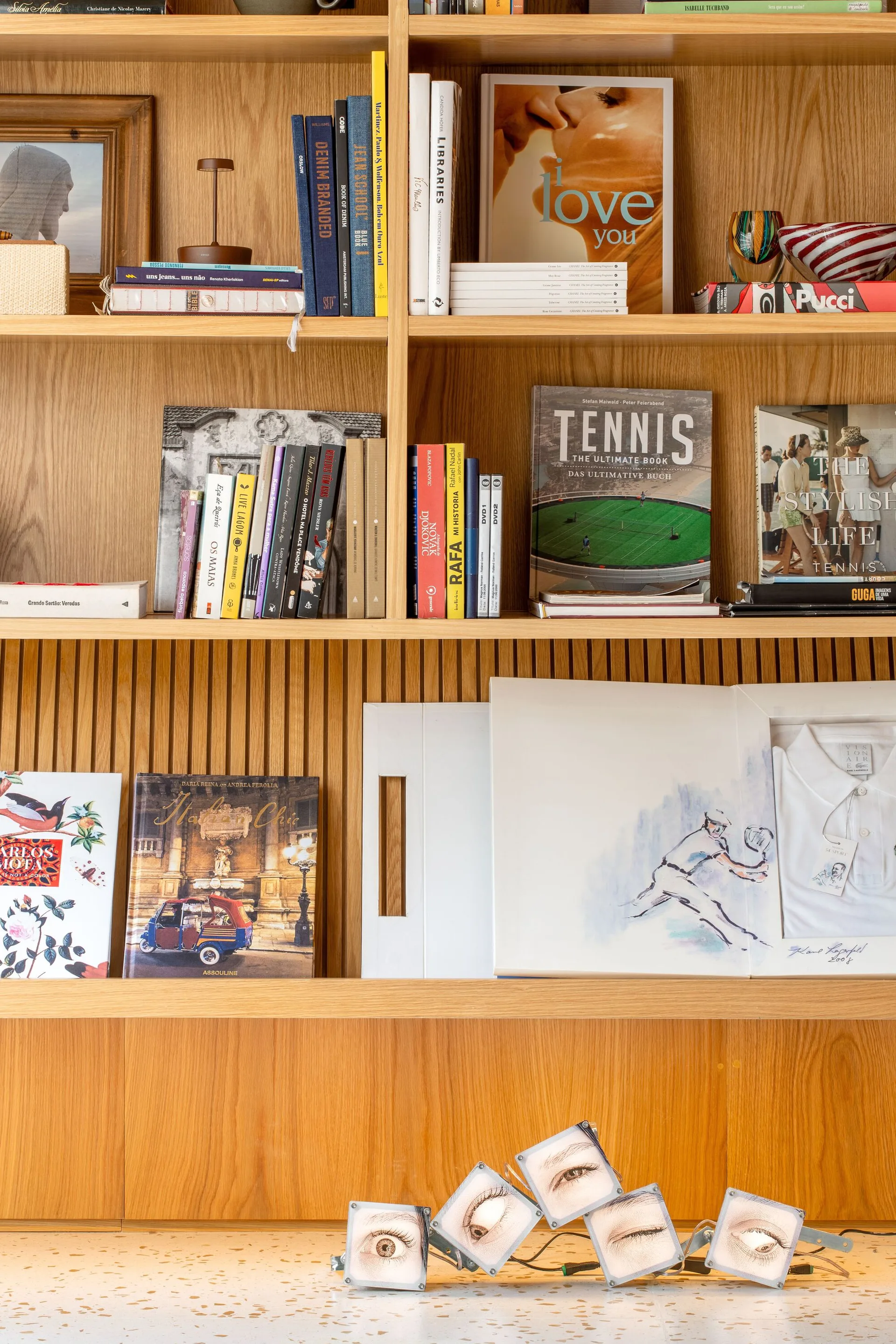 A light oak wooden bookshelf styled with books and art pieces features vertical slatted wood backing above a speckled terrazzo countertop.