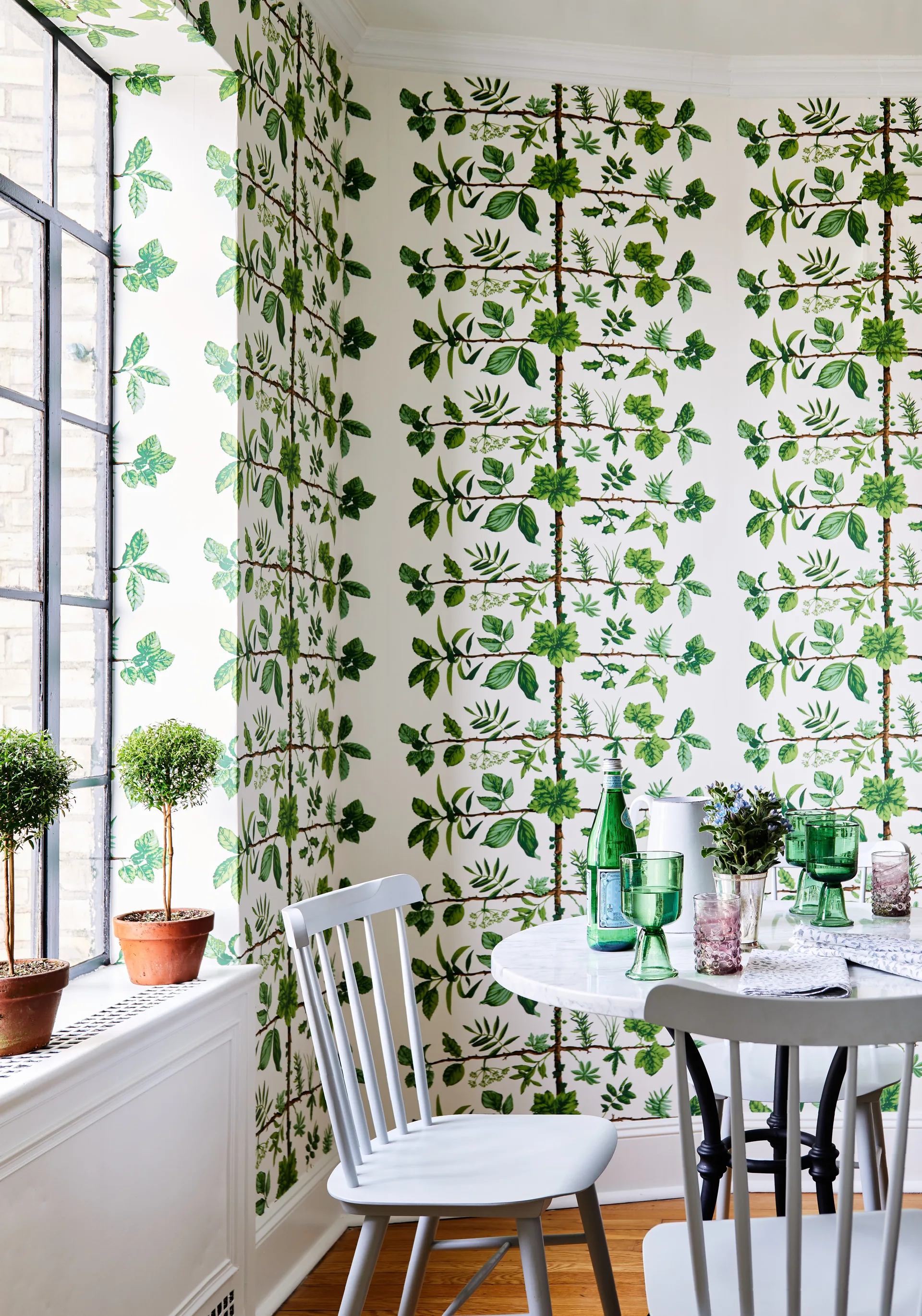 A bright dining area features a white circular table, grey spindle-back chairs, and vibrant green botanical wallpaper.