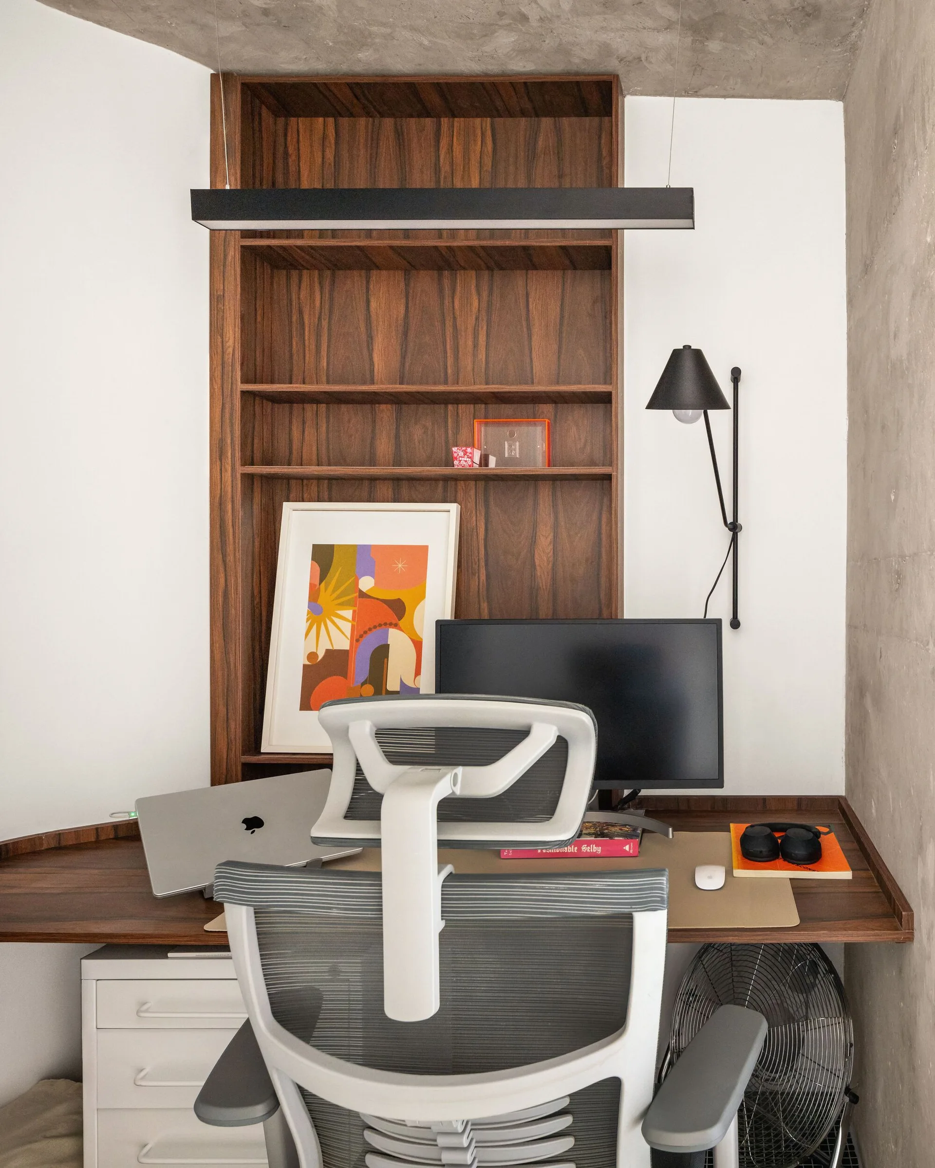 A minimalist home office featuring a built-in dark wood desk and shelving unit, an ergonomic chair, and a black linear pendant.
