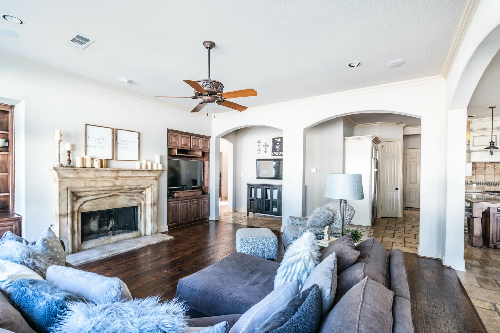 A transitional living room featuring a grey sectional sofa with textured pillows, a carved stone fireplace, and a dark wood built-in media cabinet.
