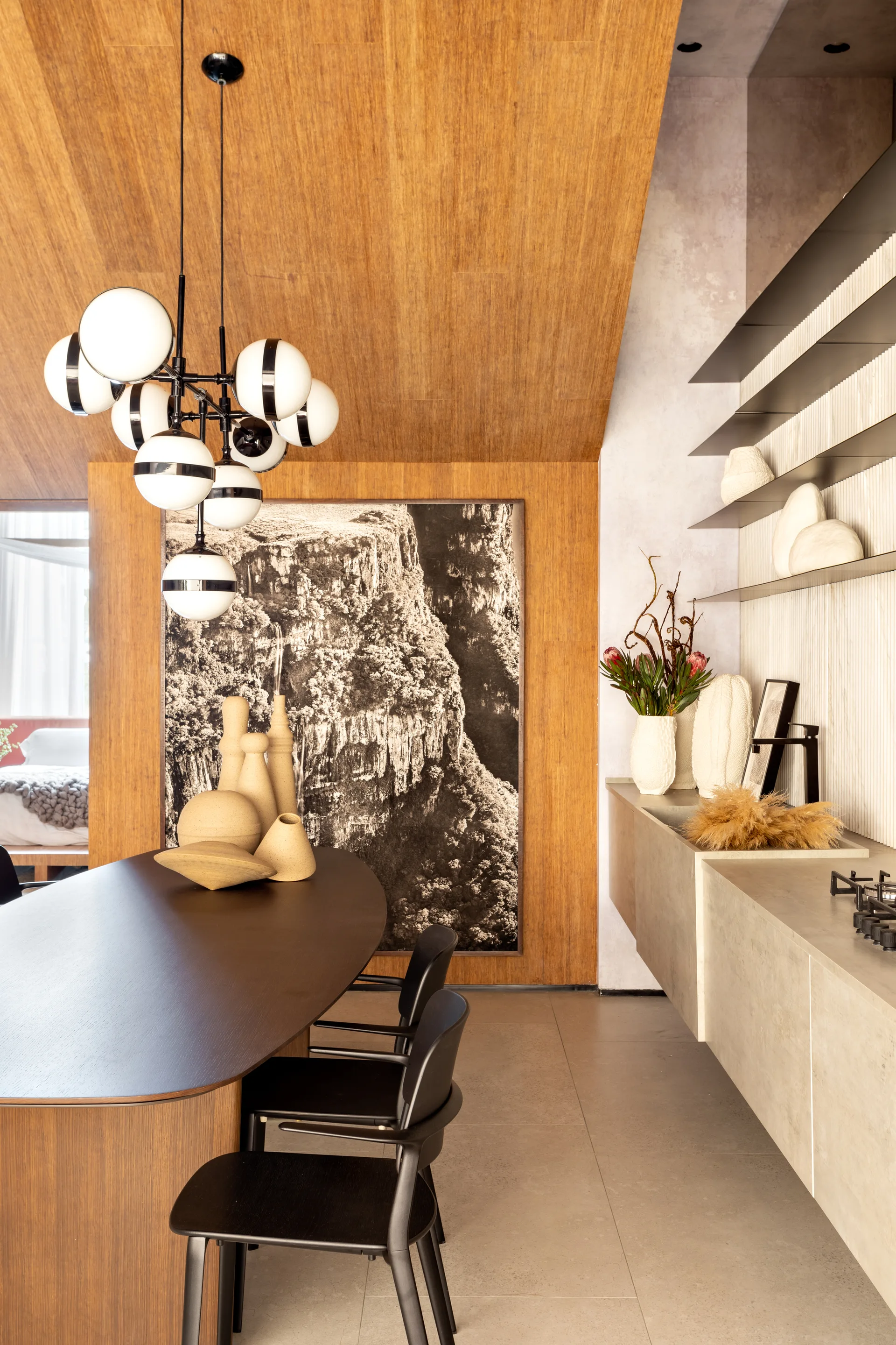A modern dining area with a dark oval table, black chairs, a multi-globe chandelier, and warm wood paneling spanning the wall and sloped ceiling.
