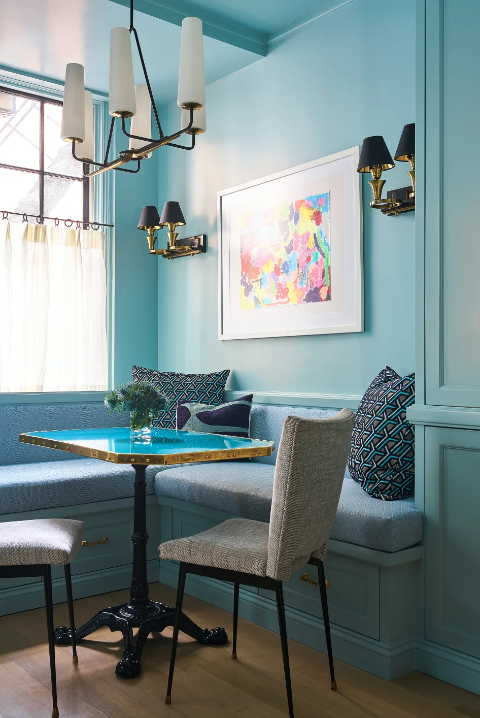 A teal breakfast nook features a built-in banquette, a blue-topped table with a brass rim, upholstered chairs, and matching painted walls and ceiling.