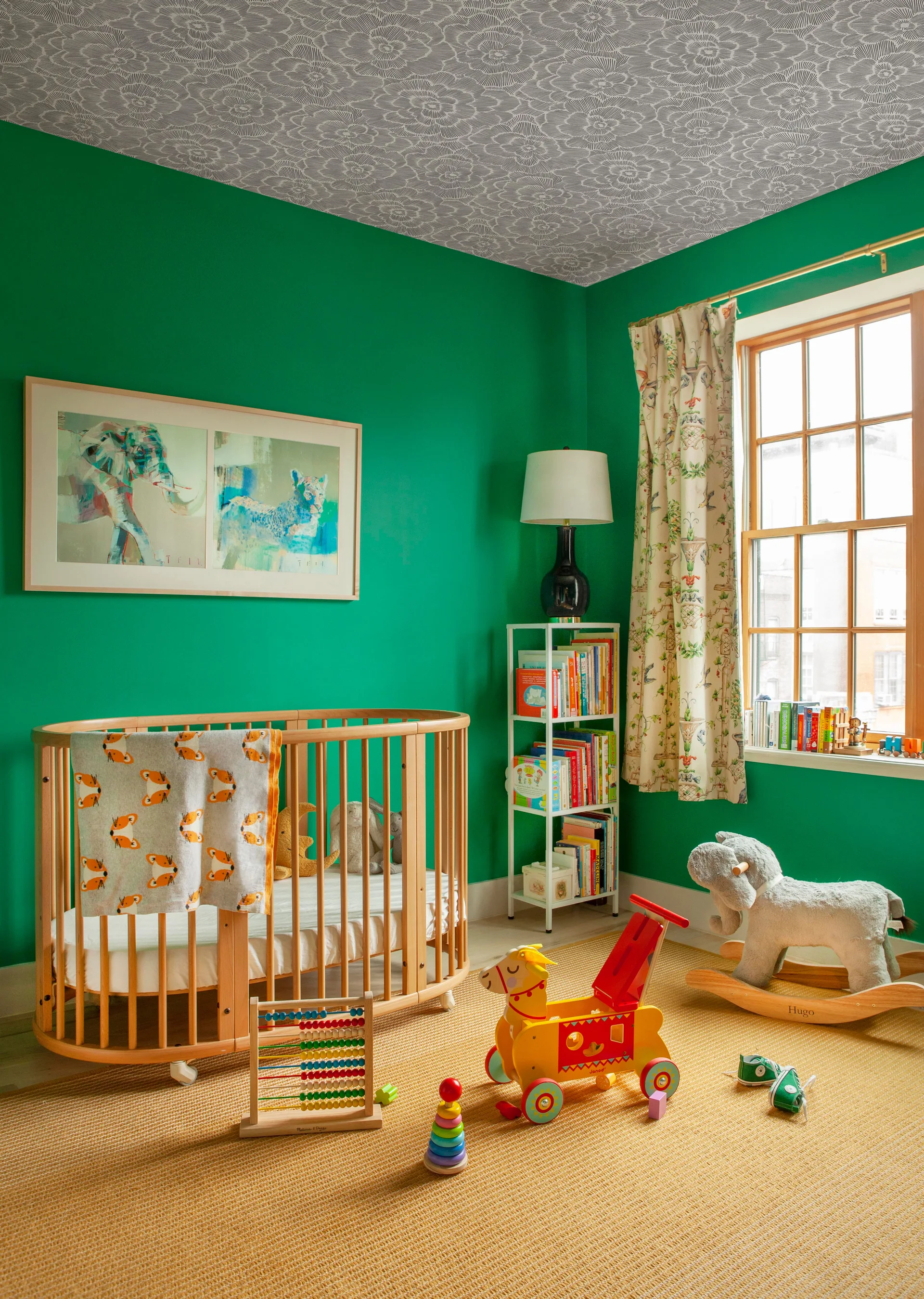 A children's nursery features vibrant green walls, an oval wooden crib, and a patterned ceiling above a tan textured rug.
