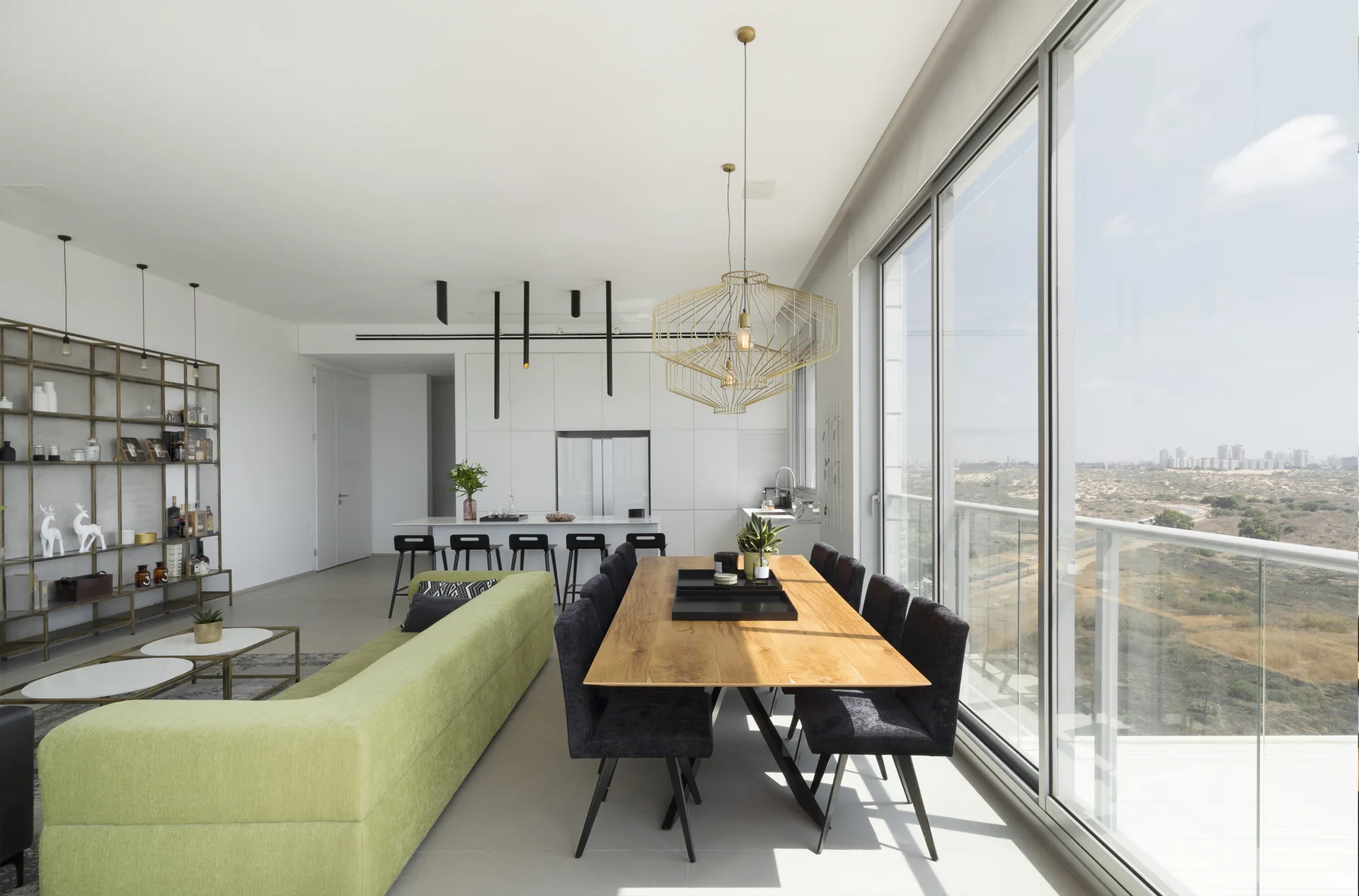 An open-concept living and dining room features a light green sofa, a long wooden table with dark chairs, and floor-to-ceiling windows.