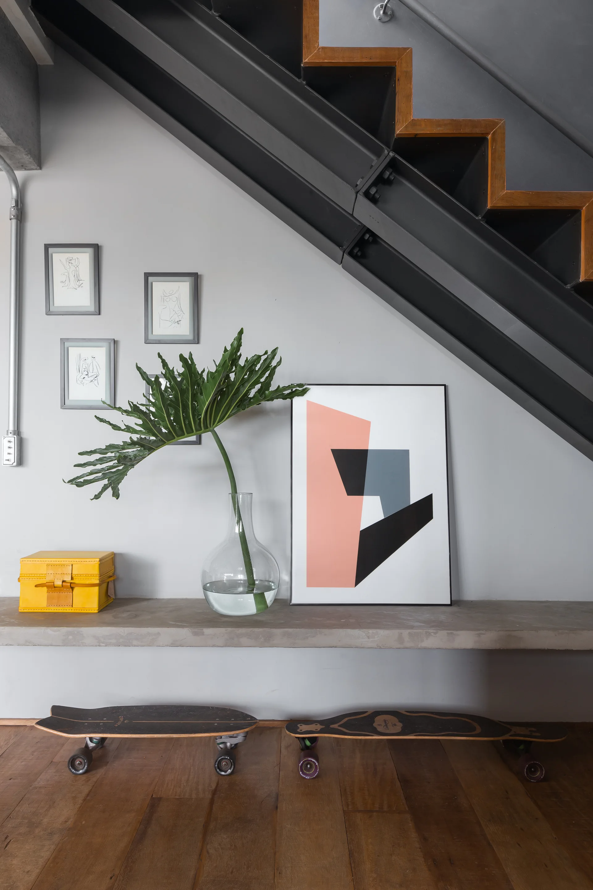 A minimalist entryway features a black metal industrial staircase over a concrete floating ledge styled with a green leaf in a vase and abstract art.