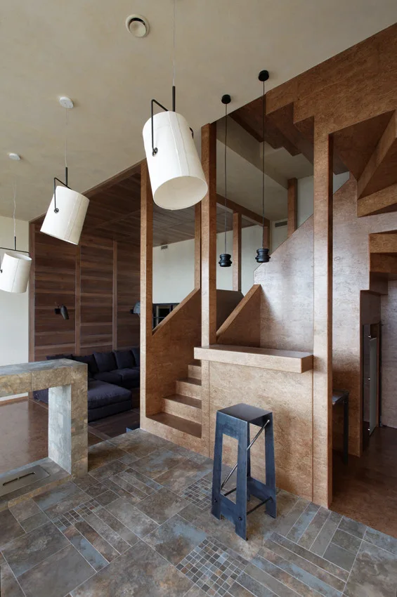 An interior featuring a warm wood staircase with an integrated bar ledge, a metal bar stool, stone tile flooring, and white bucket-style pendant lights.