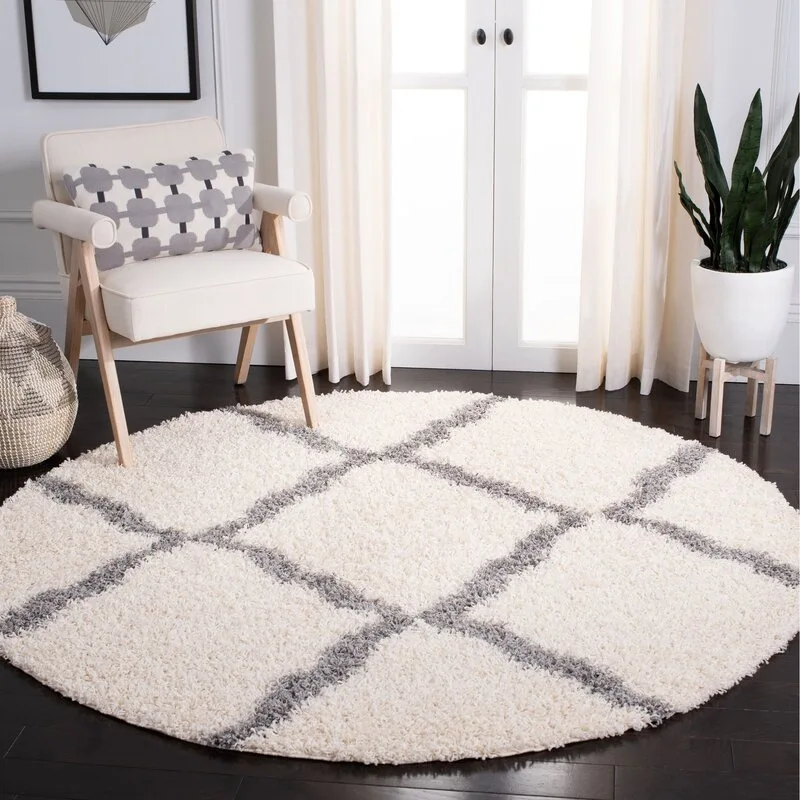 A round cream shag rug with a gray grid pattern sits on a dark wood floor near a white armchair and a potted plant.