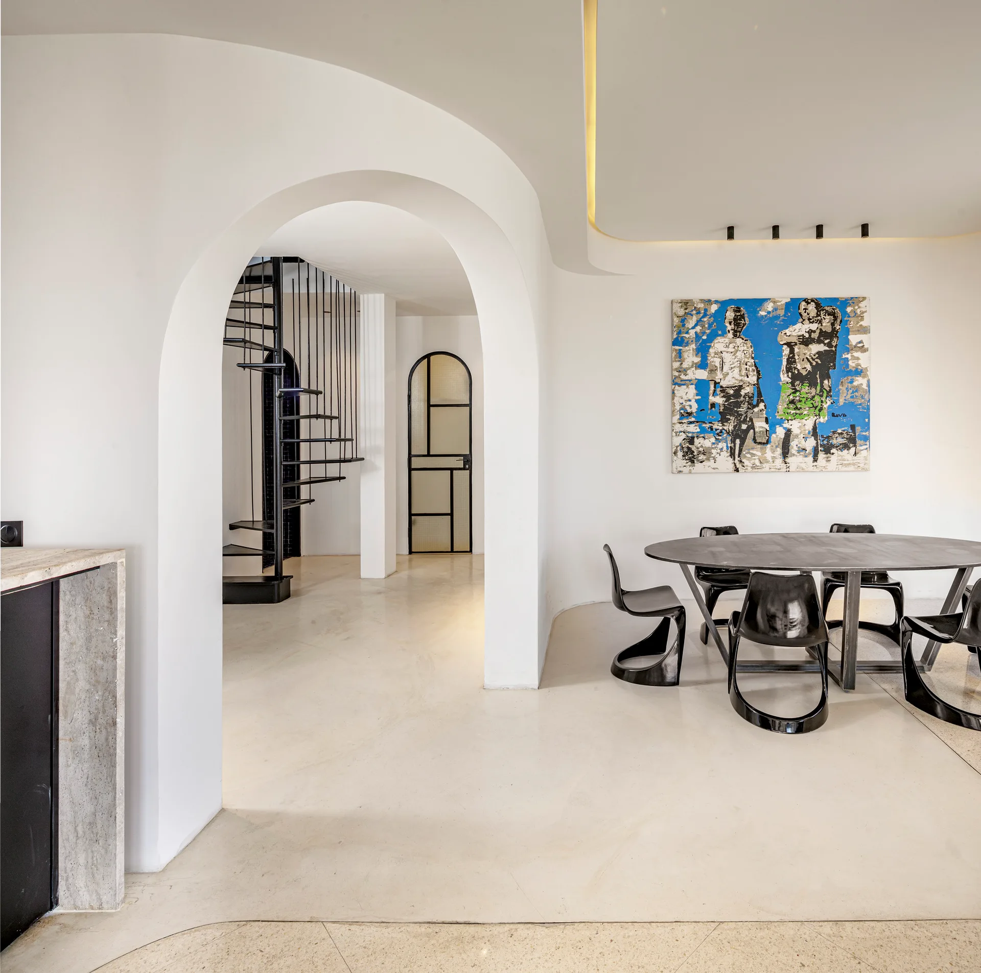 A minimalist white dining room features a black table and sculptural chairs next to an arched opening revealing a black spiral staircase.