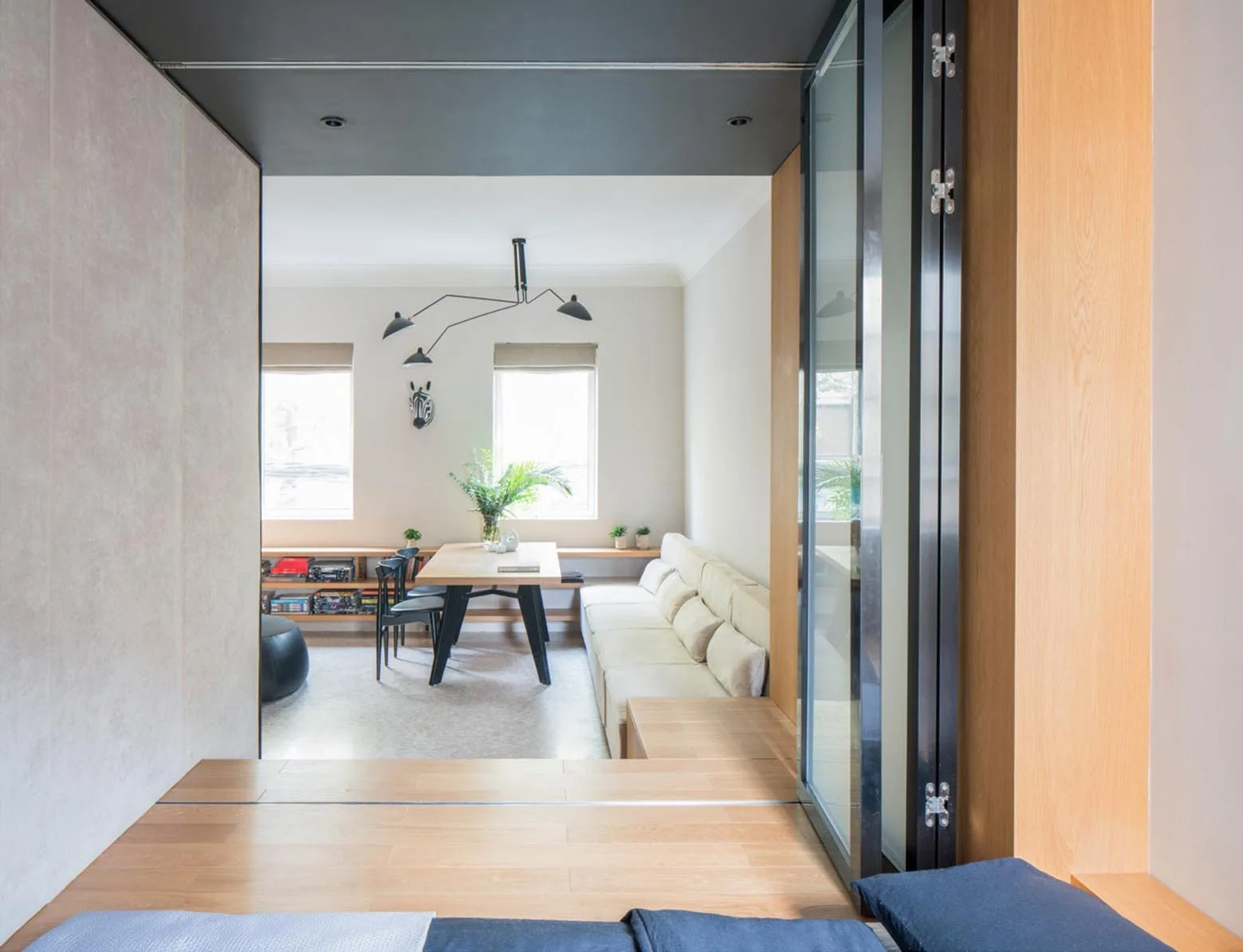 A view from a raised wooden landing looking into a bright living and dining room with a long cream sofa, a light wood dining table, and black accents.
