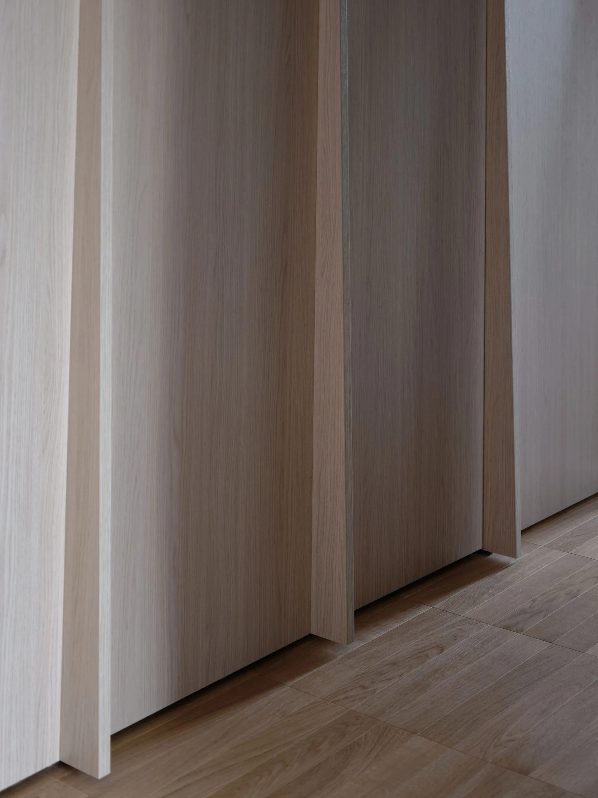 Close-up of vertical light beige wood wall panels with stepped edges meeting a light-toned wood plank floor.
