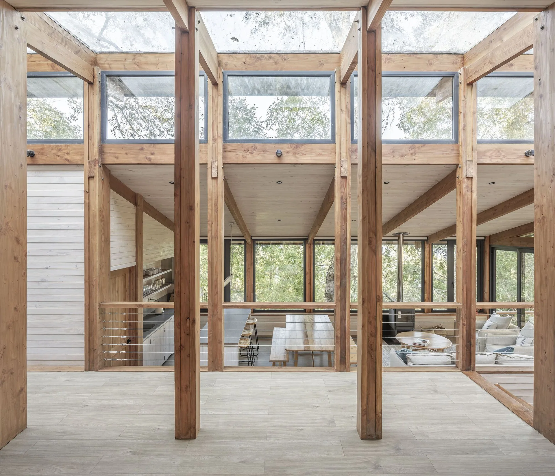 A modern cabin interior featuring a multi-level timber-frame structure, clerestory windows, wooden beams, and a view of the open-plan living area below.