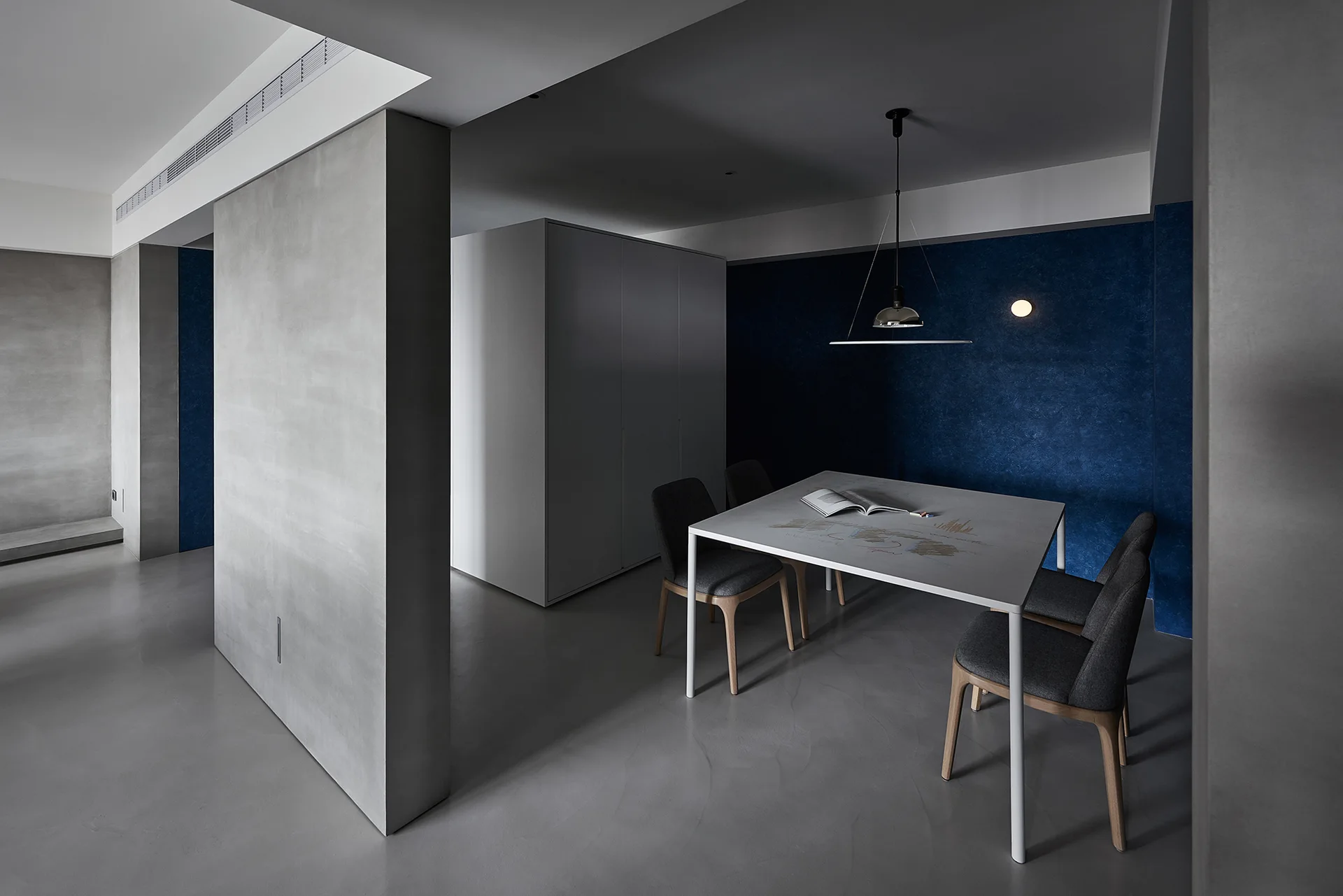 A minimalist dining room with grey walls, a textured blue accent wall, a white table, and grey upholstered chairs.
