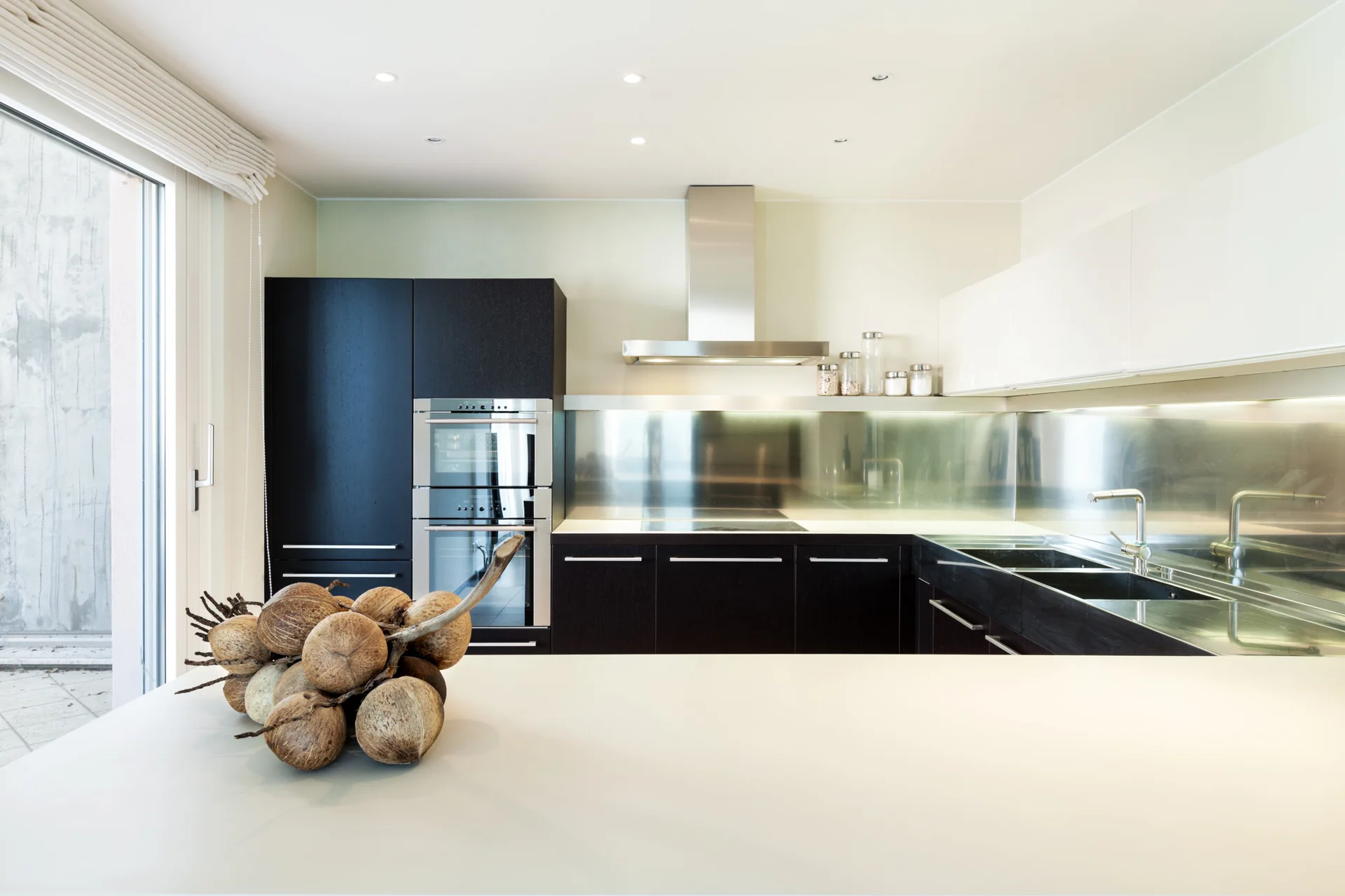 A modern kitchen features matte black base cabinets, a stainless steel backsplash, and glossy white upper cabinetry.