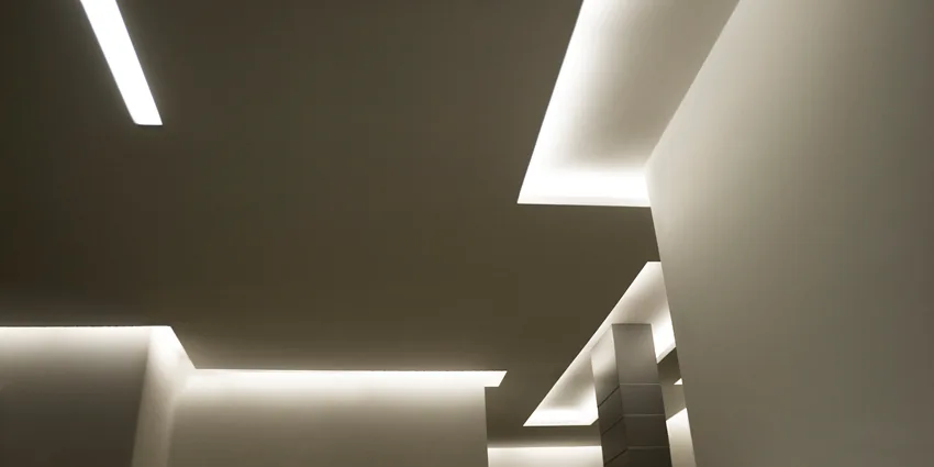 An architectural view of a tiered white ceiling featuring recessed warm cove lighting with sharp geometric angles.