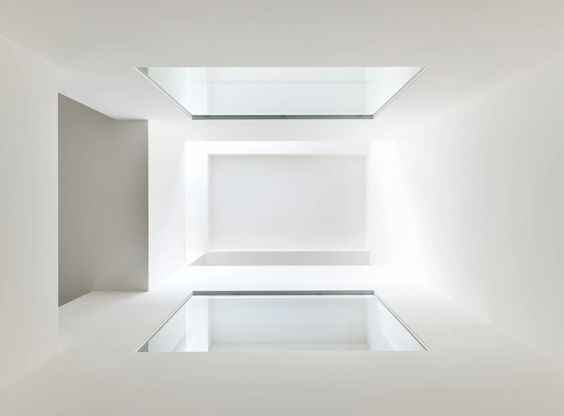 A minimalist white architectural stairwell looking up through two symmetrical rectangular skylights set in smooth plaster.