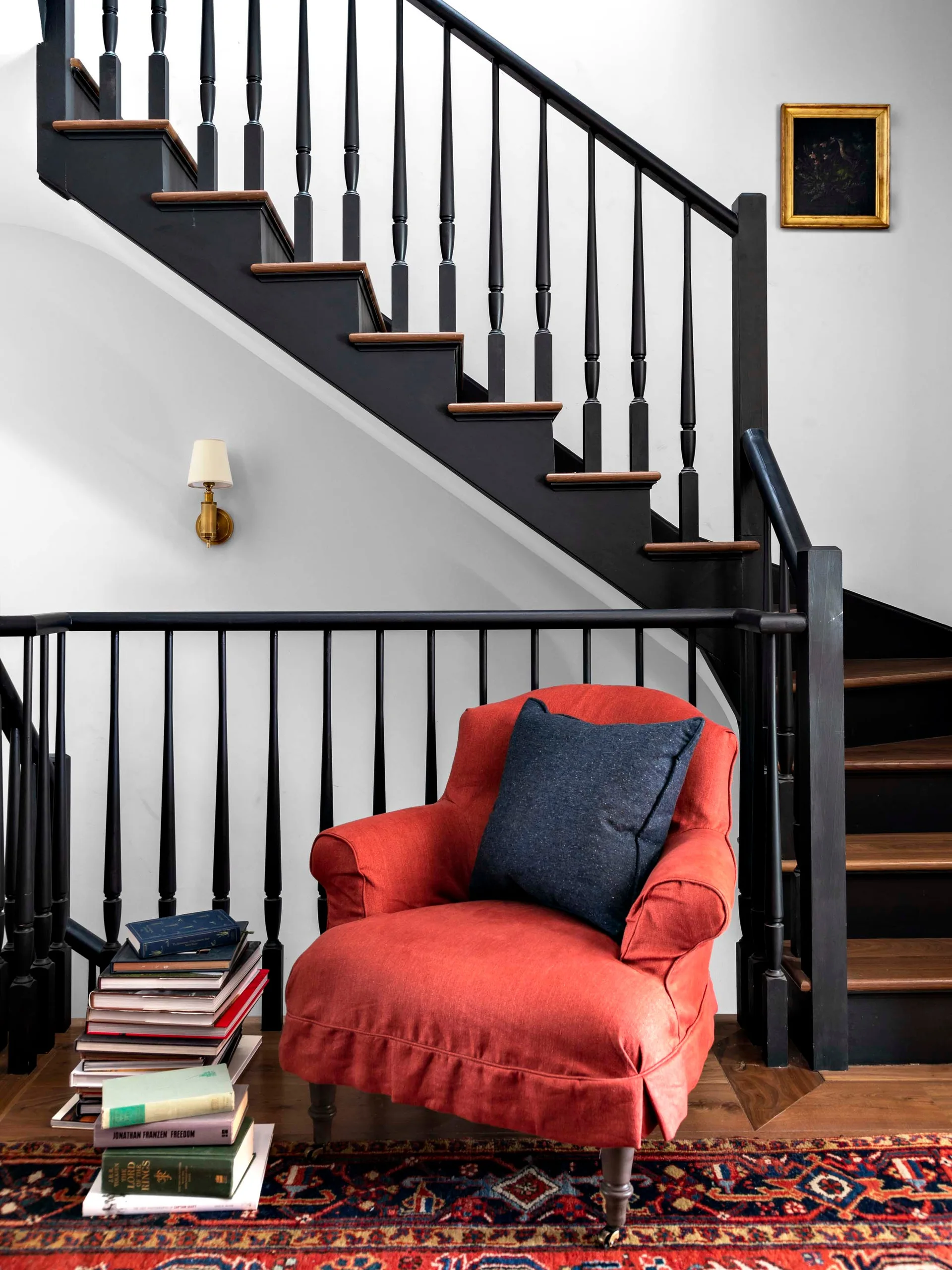 A red upholstered armchair sits next to a black painted wooden staircase with wood treads.