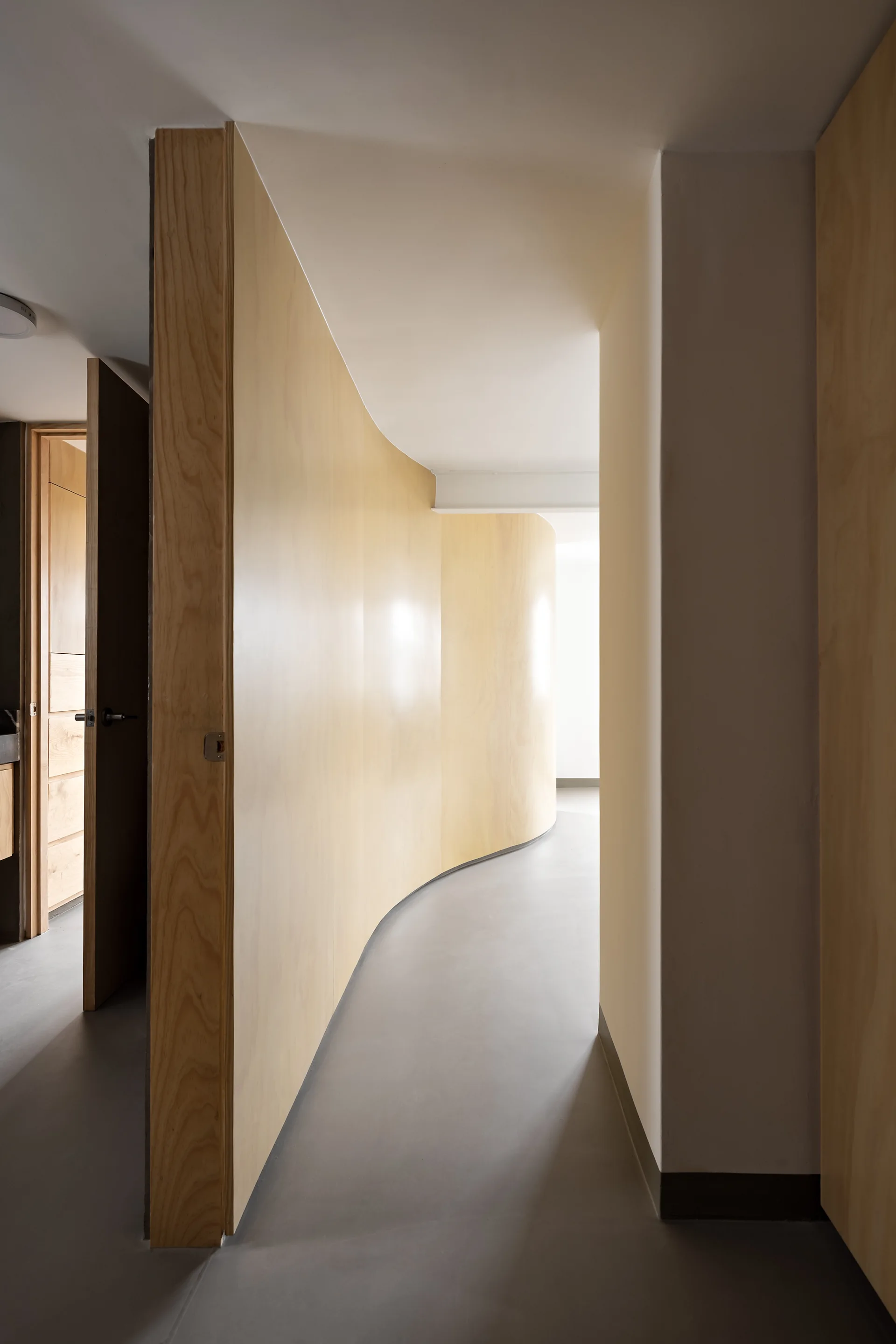 A minimalist hallway with a long curved light wood paneled wall and a smooth matte gray floor.