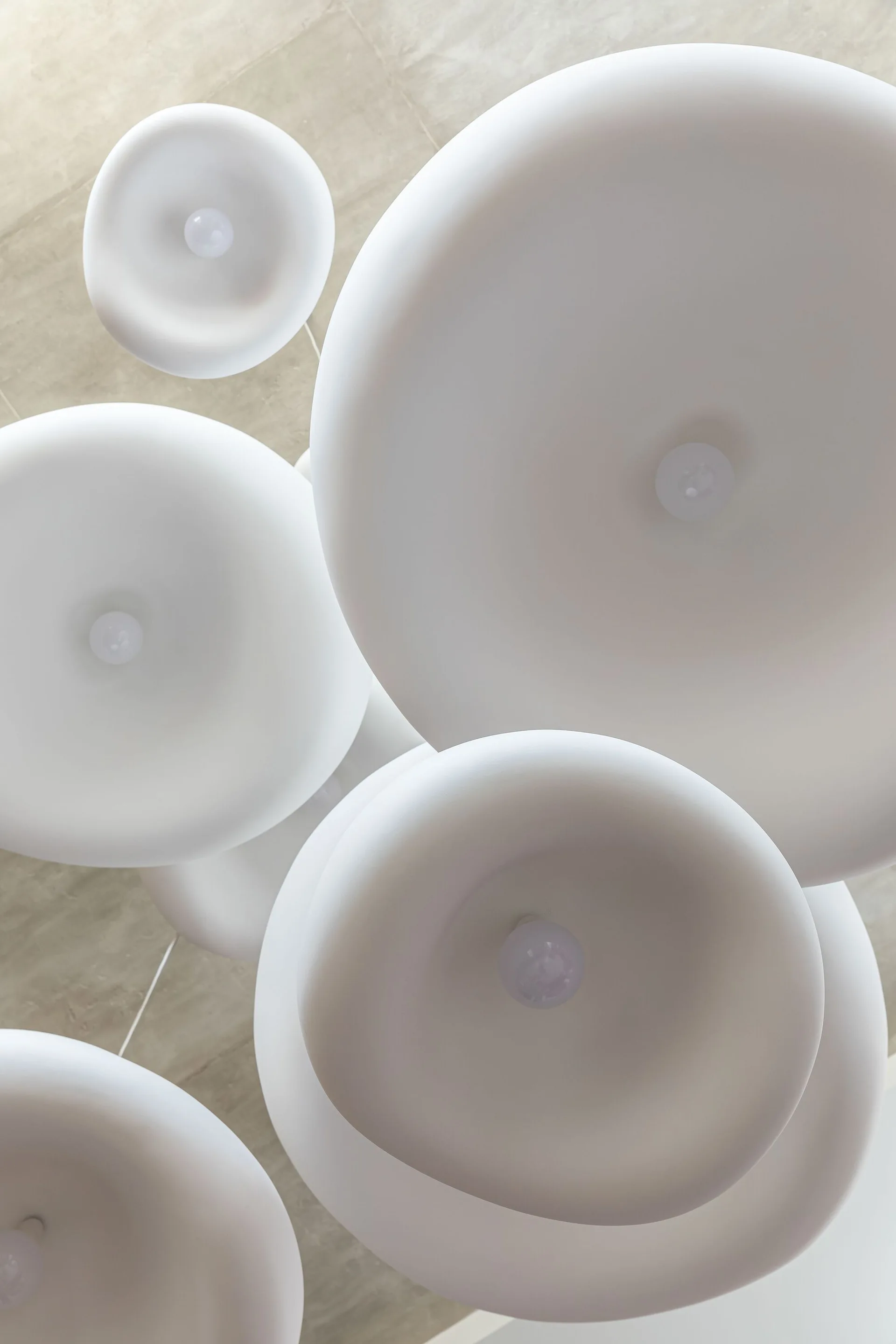 A low-angle view of multiple matte white disc-shaped pendant light fixtures hanging from a light neutral ceiling.