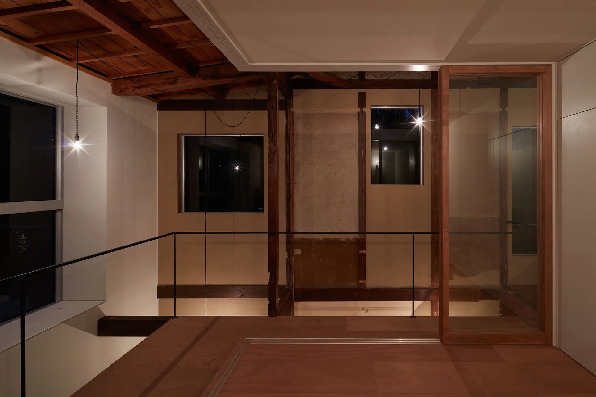 A modern landing features exposed timber rafters, warm pendant lights, a black railing, and a wood-framed glass sliding door.
