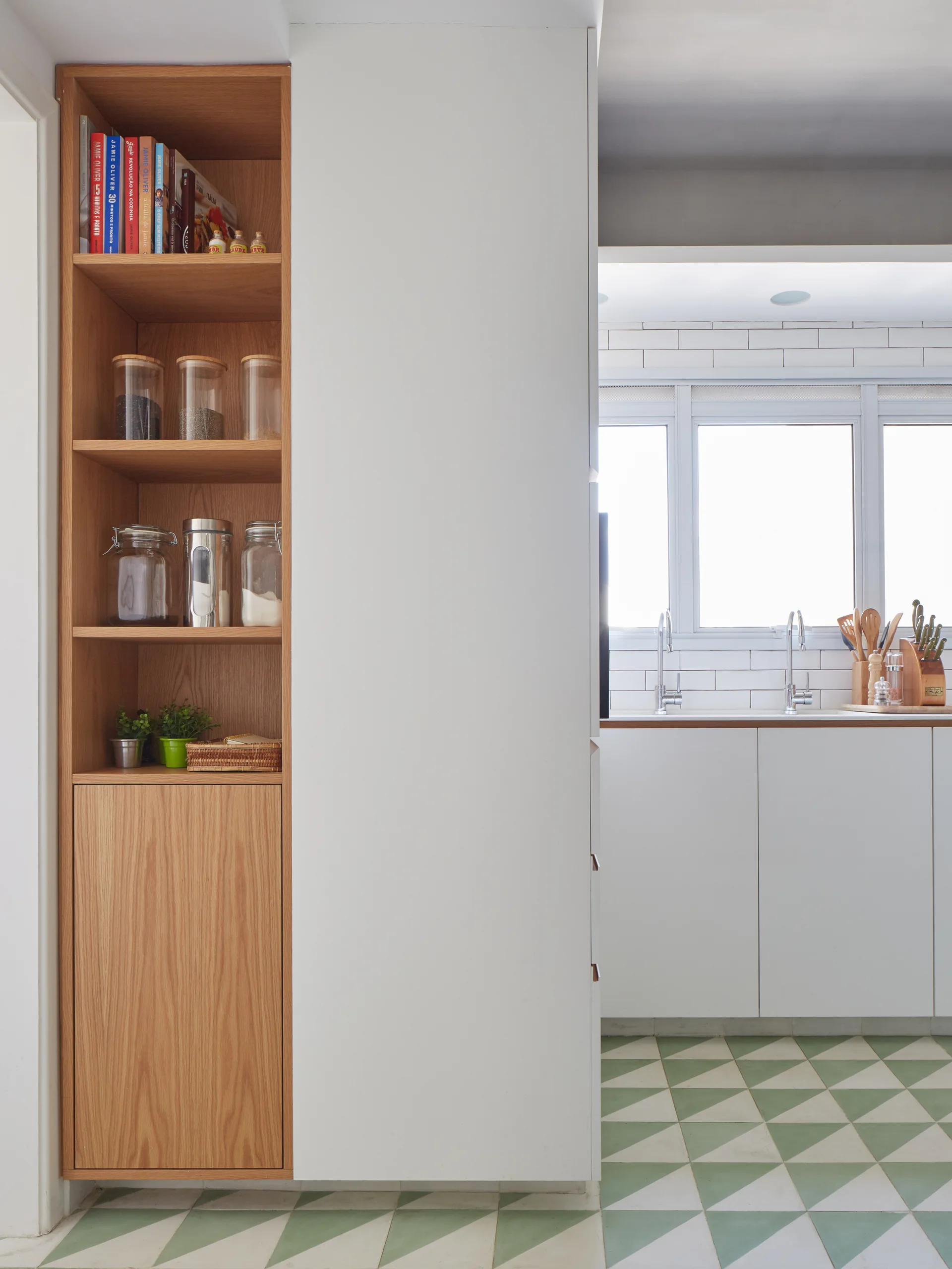 A modern kitchen featuring a tall wood pantry next to white cabinets, with green and white geometric floor tiles and a subway tile backsplash.
