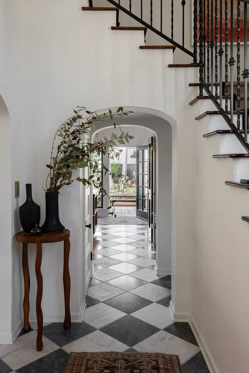 An entryway foyer featuring black and white checkerboard flooring, a wooden staircase, and an arched doorway leading to a glass door.