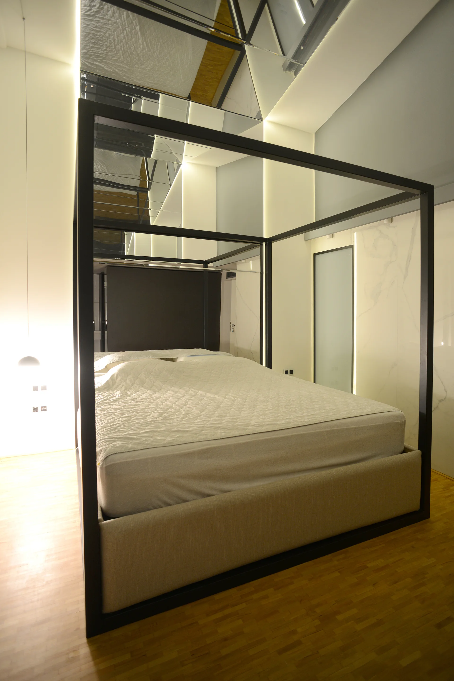 A minimalist black metal canopy bed sits in a modern bedroom with white marble wall panels, wood flooring, and a mirrored ceiling reflecting the room.