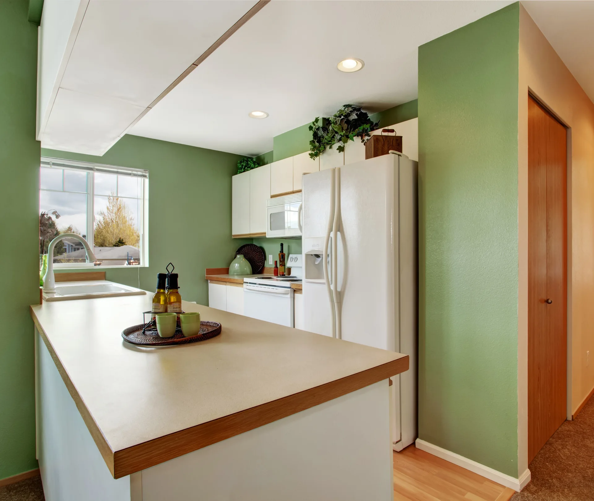 A residential kitchen features sage green walls, white appliances, and a white kitchen island with a wood-trimmed countertop.