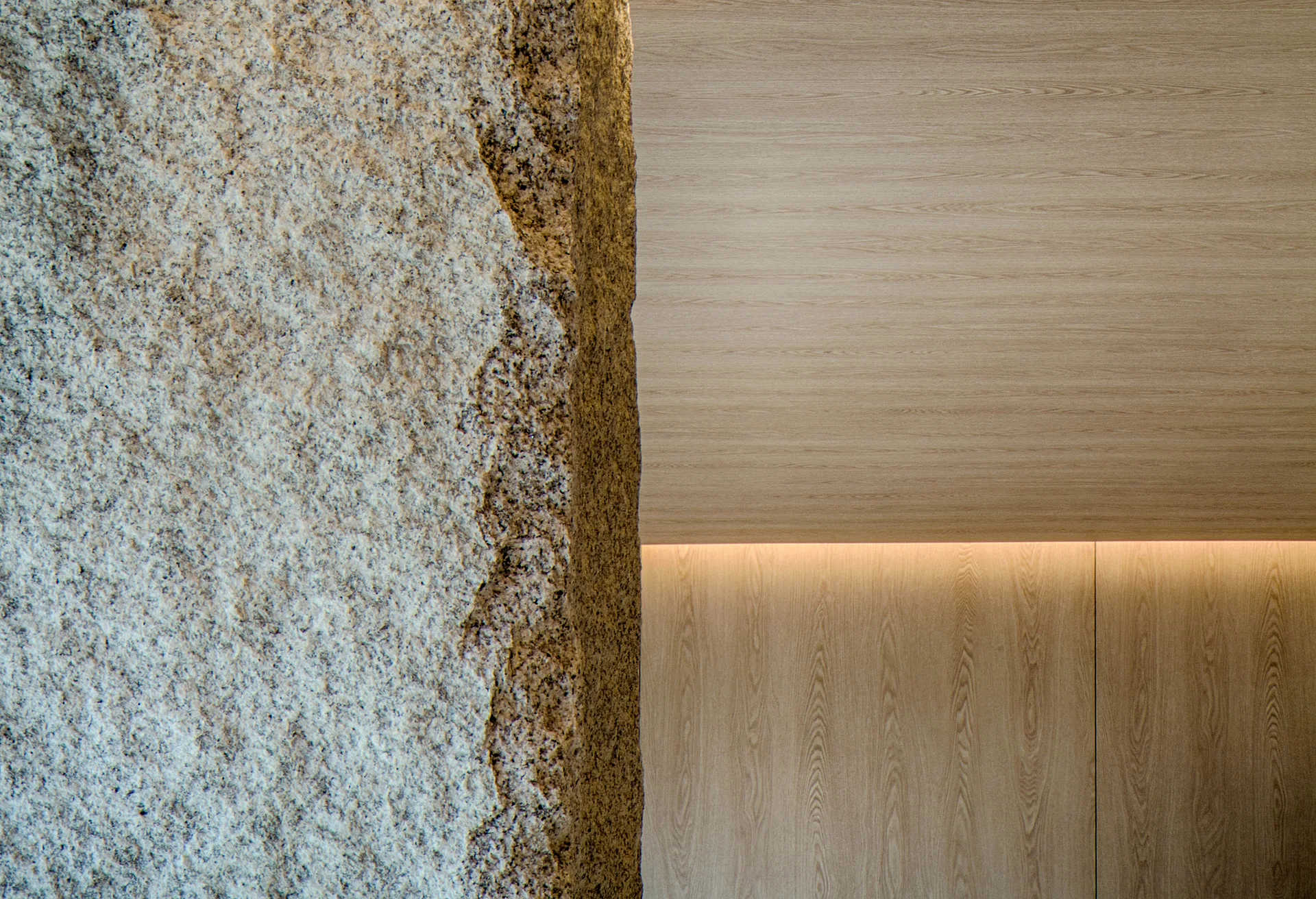 A close-up of a wall featuring rough natural stone on the left and smooth light wood paneling with integrated cove lighting on the right.