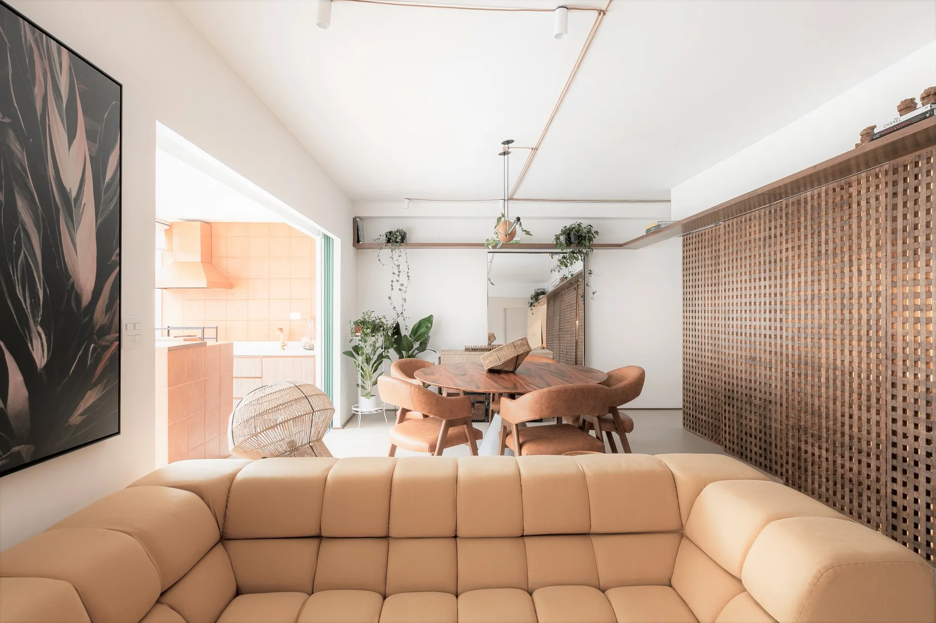A bright modern living and dining area featuring a tan tufted sofa, a round wooden table, and a wood grid lattice wall screen.