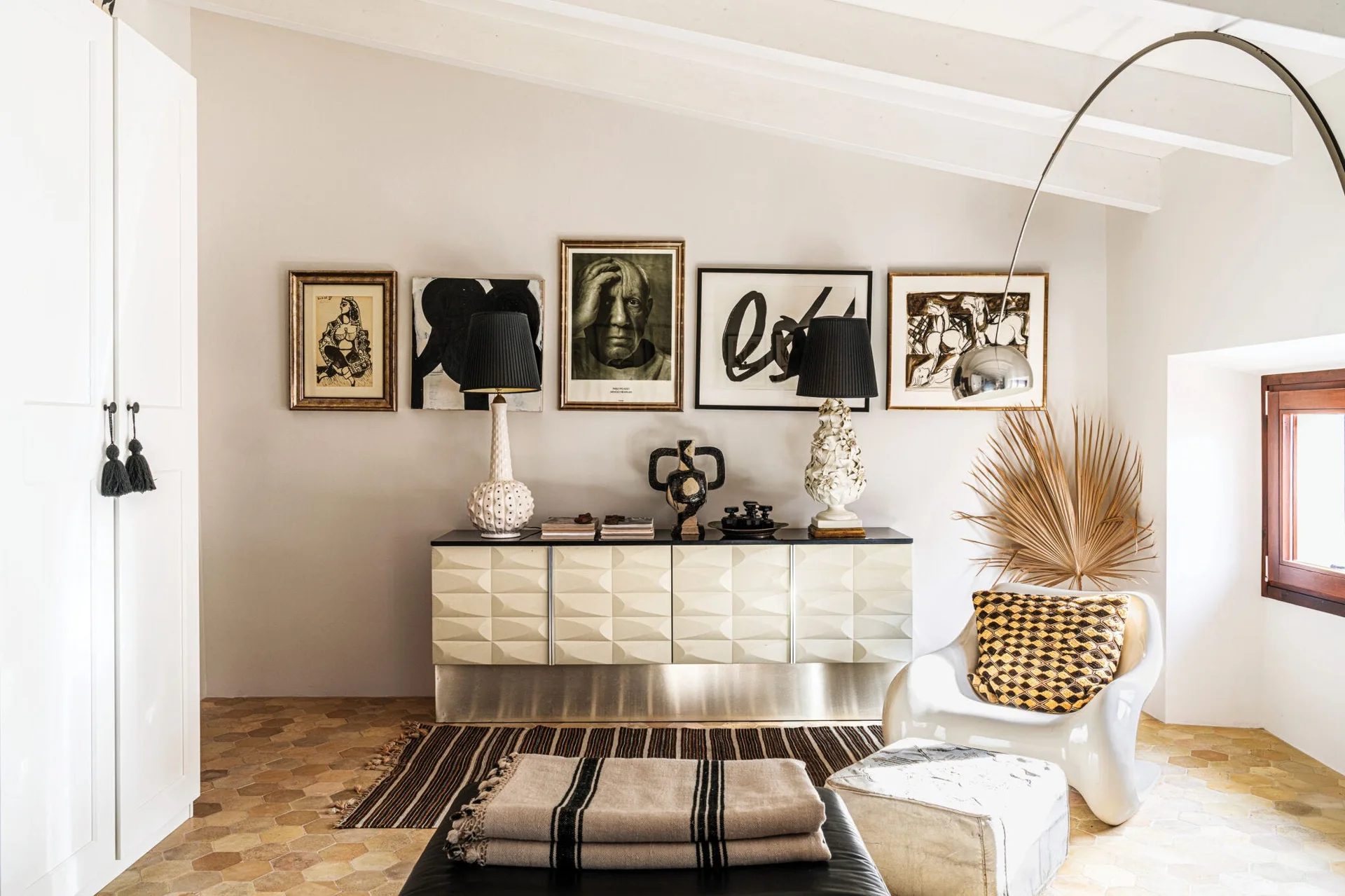 A living room features a textured geometric sideboard beneath a gallery wall of art, resting on terracotta hexagonal tile flooring.