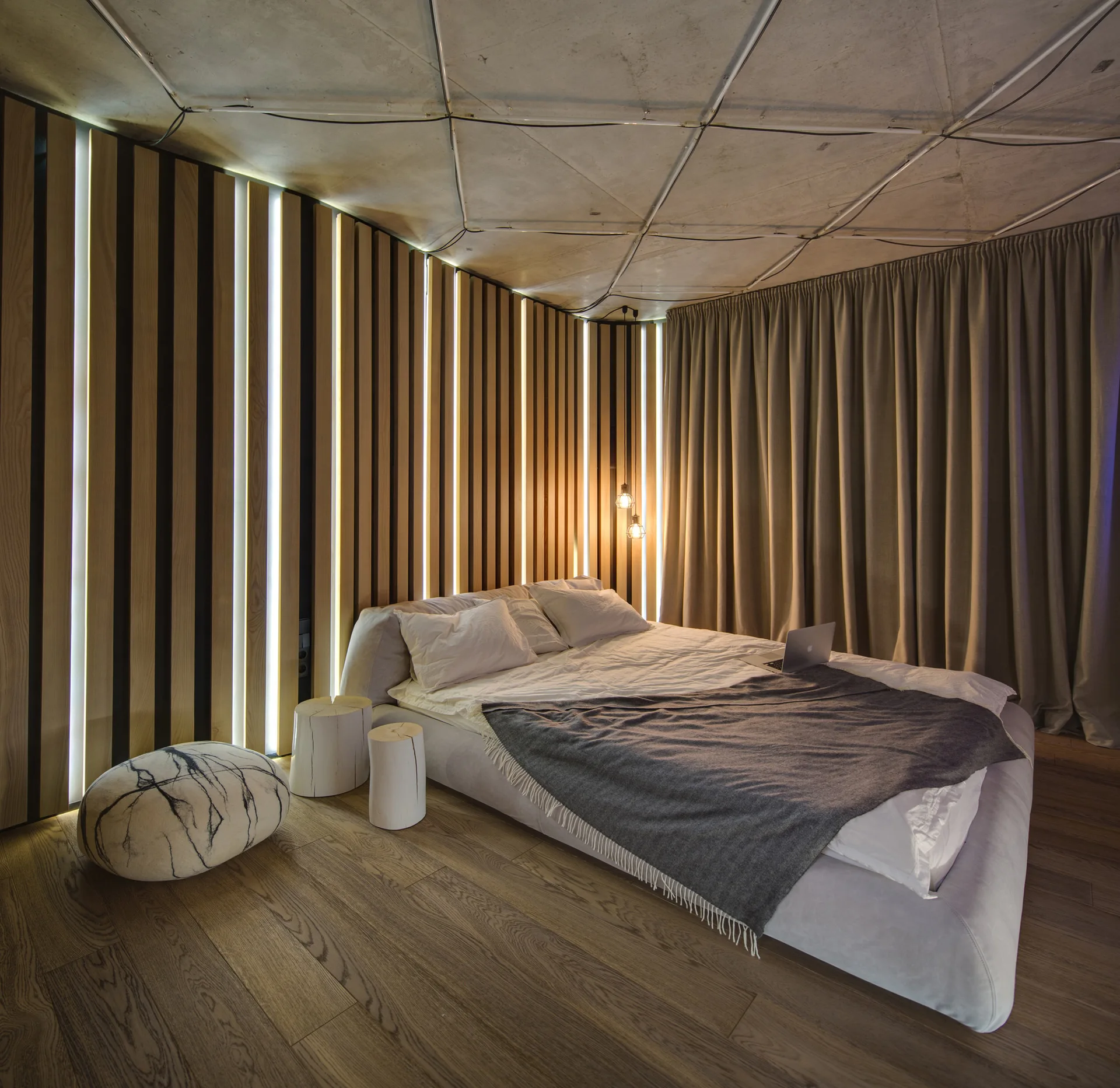 A modern bedroom features a low-profile bed against a vertical wood slat wall with integrated vertical light strips and a geometric ceiling.