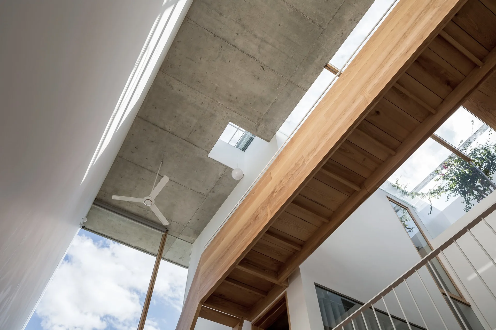 Looking up at a light-toned wooden floating staircase beneath an exposed grey concrete ceiling with small square skylights.
