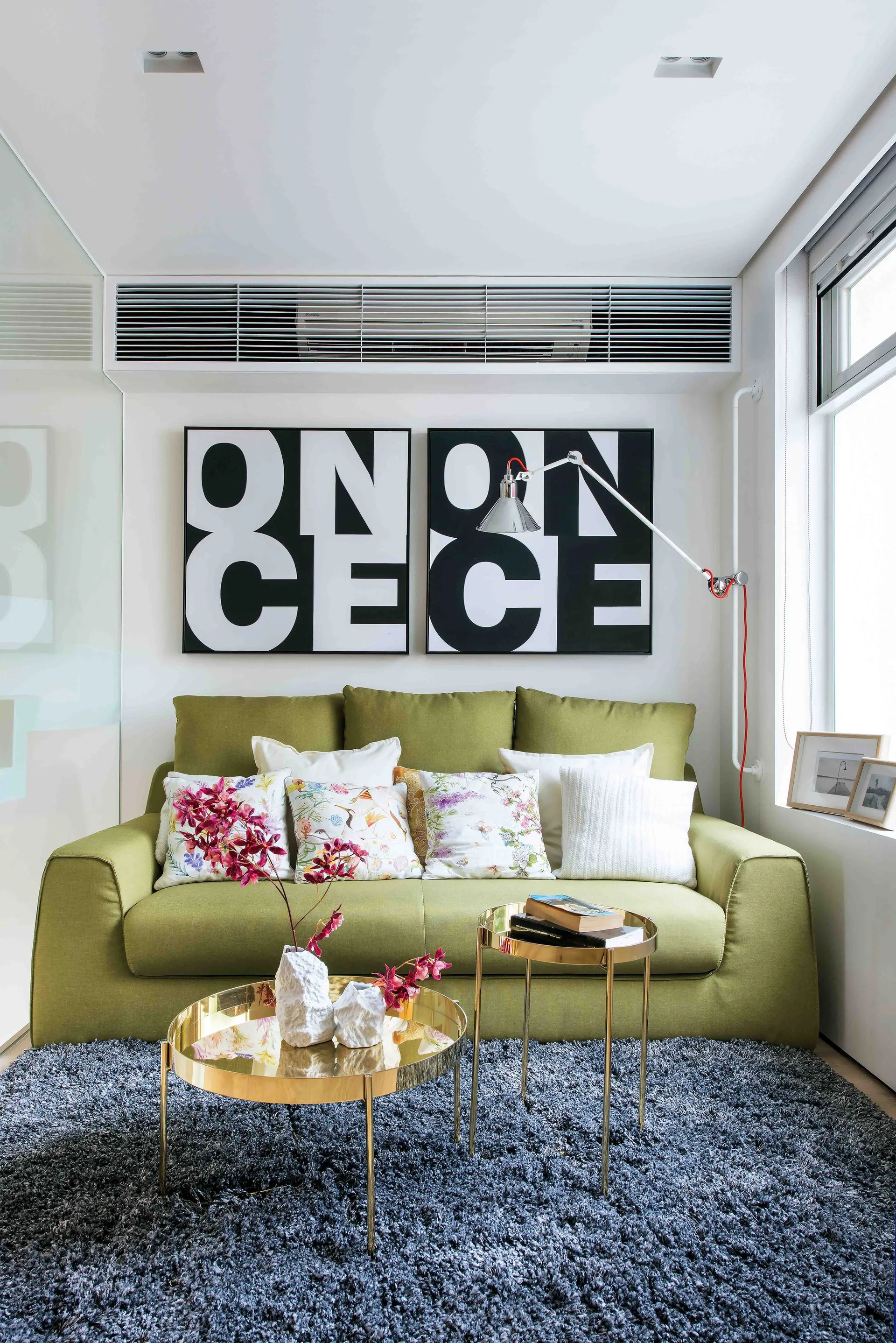 A modern living room features an olive green sofa under black and white typographic art, paired with two gold nesting coffee tables on a grey shaggy rug.