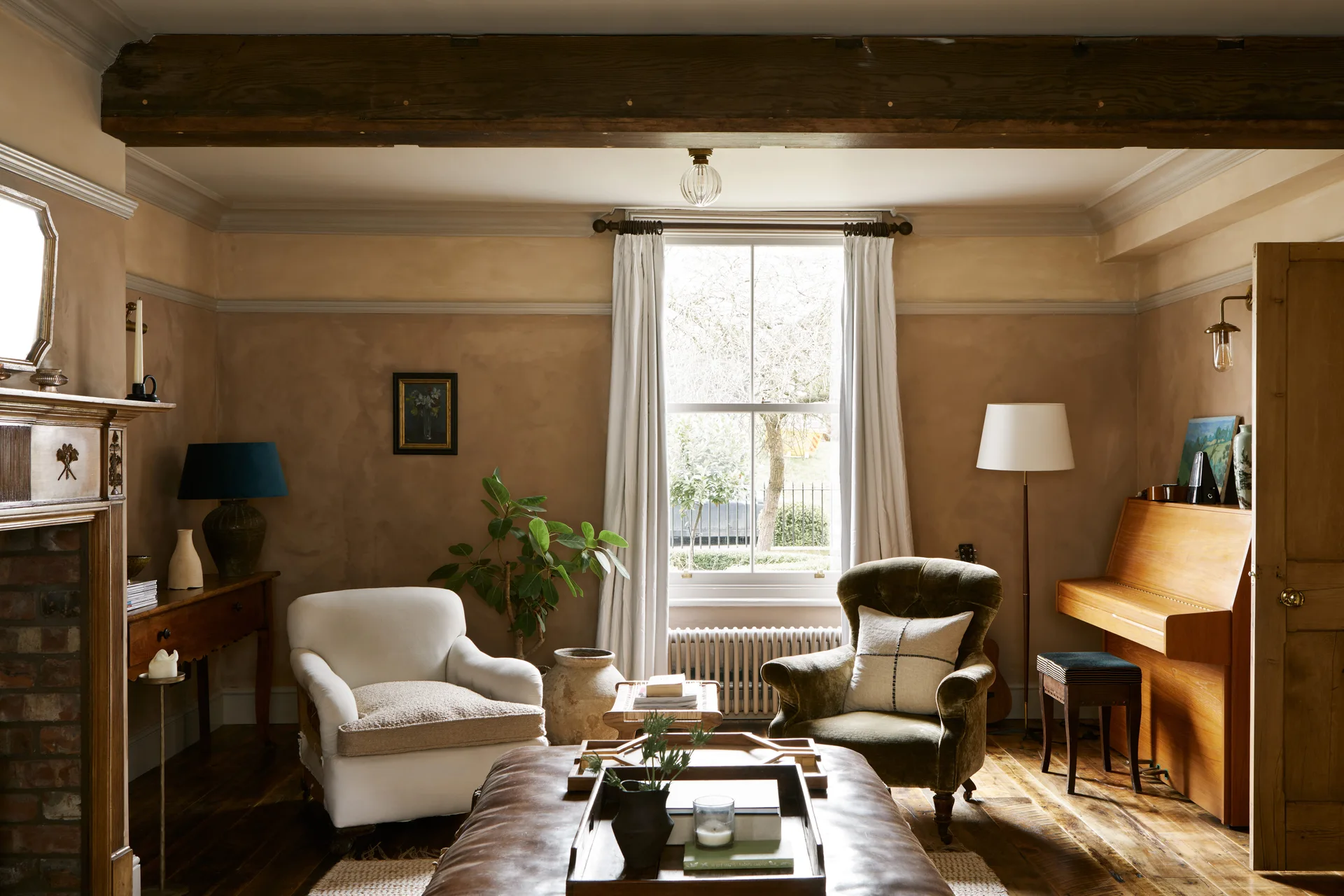 A living room featuring textured plaster walls, two upholstered armchairs, an upright wooden piano, and a central leather ottoman.